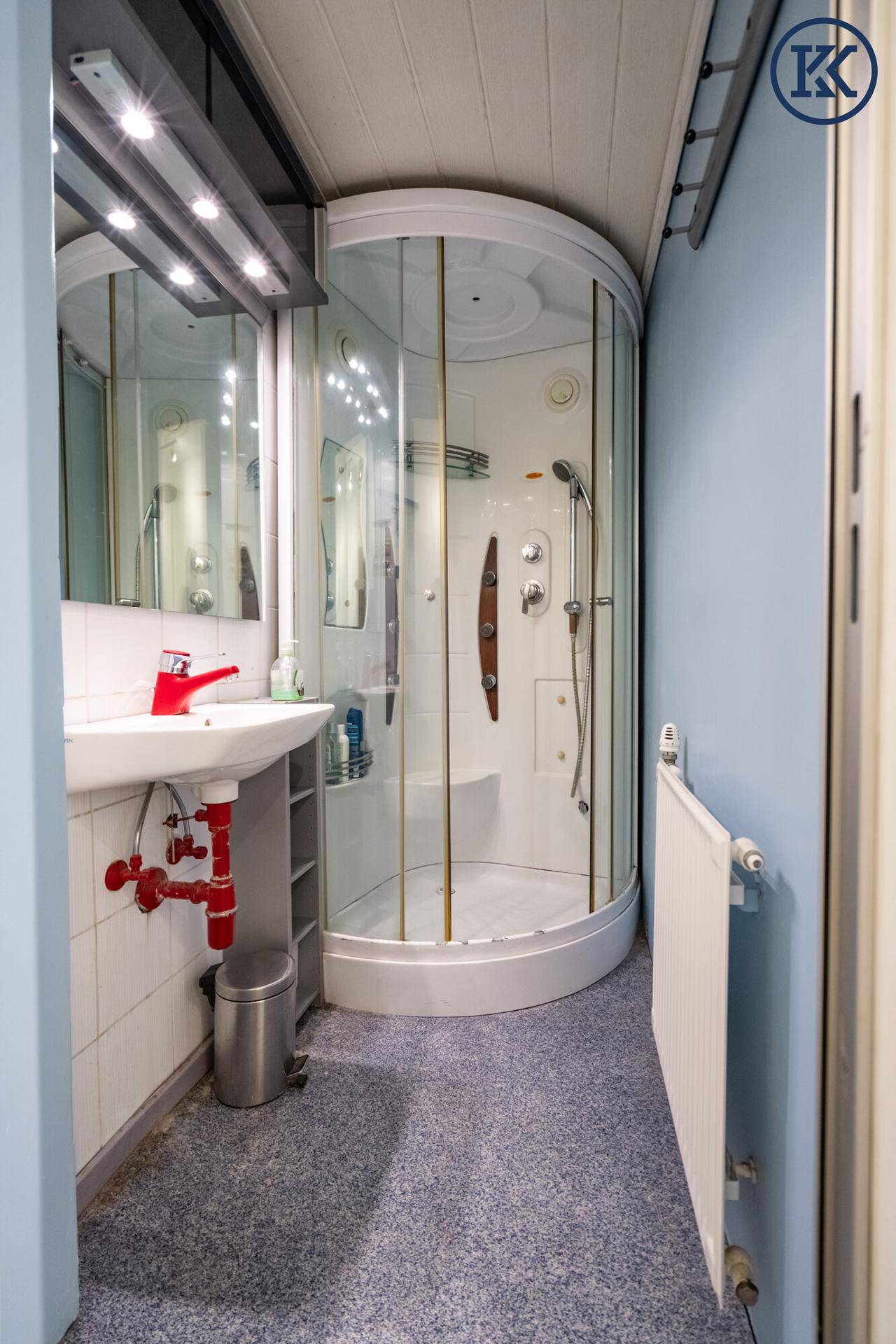 Kleines Badezimmer mit Eckduschkabine, Einzelwaschbecken und Heizkörper, in hellblauen Farbtönen.