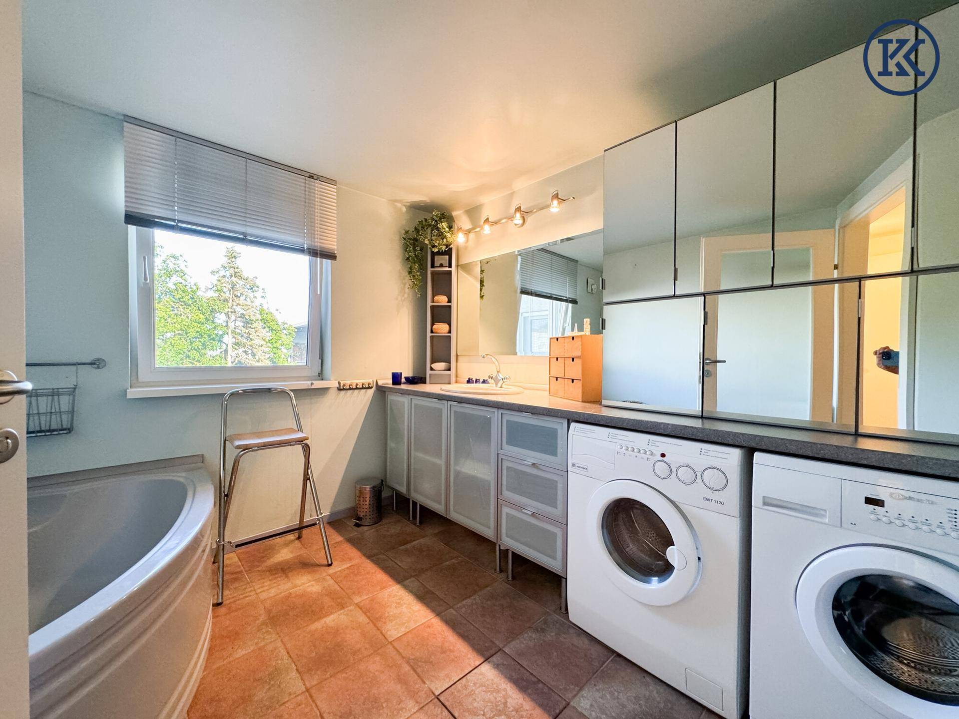 Helles Badezimmer mit Fenster, Badewanne, Einzelwaschbecken und integrierten Waschmaschinen.