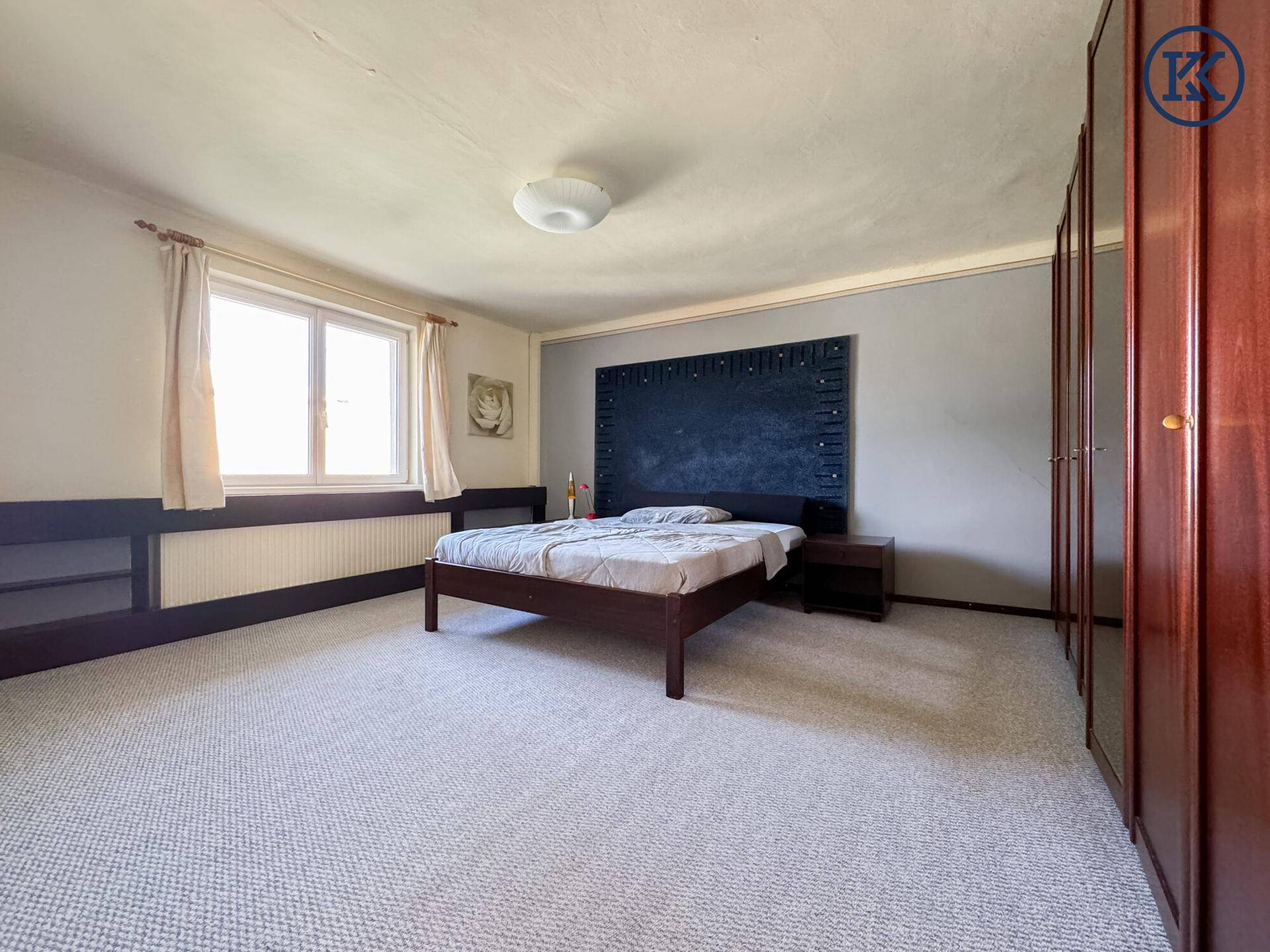 Geräumiges Schlafzimmer mit grauem Teppichboden, Doppelbett und großen Holzschränken.