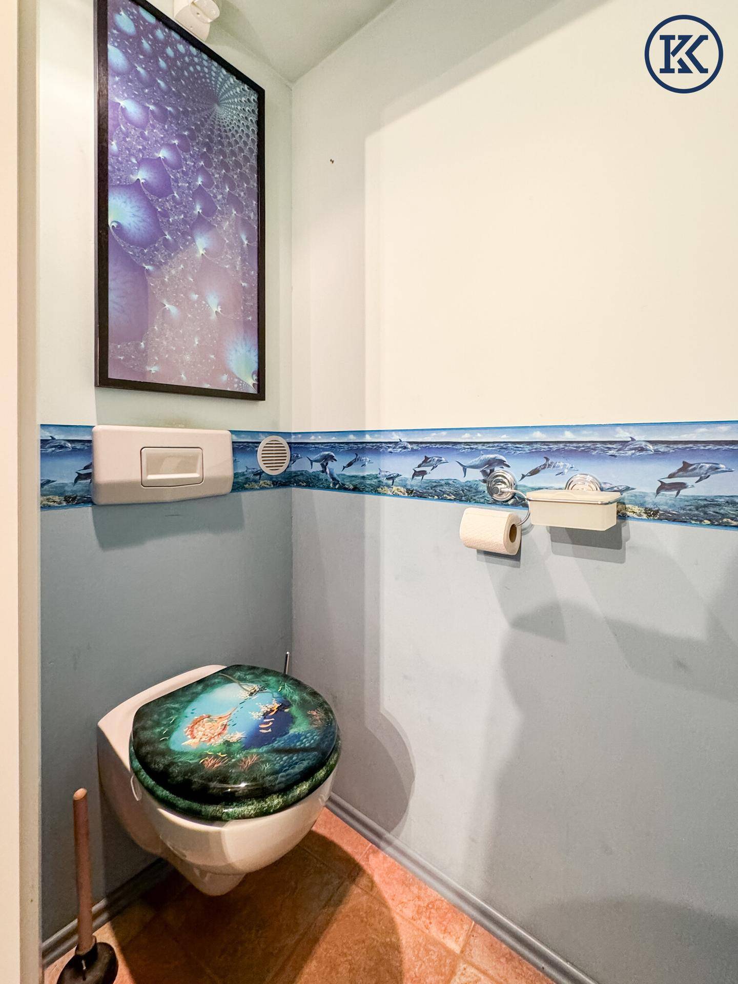 Kleines WC mit blauen Wänden, dekorativer Bordüre und einem einzigartig gestalteten Toilettensitz.