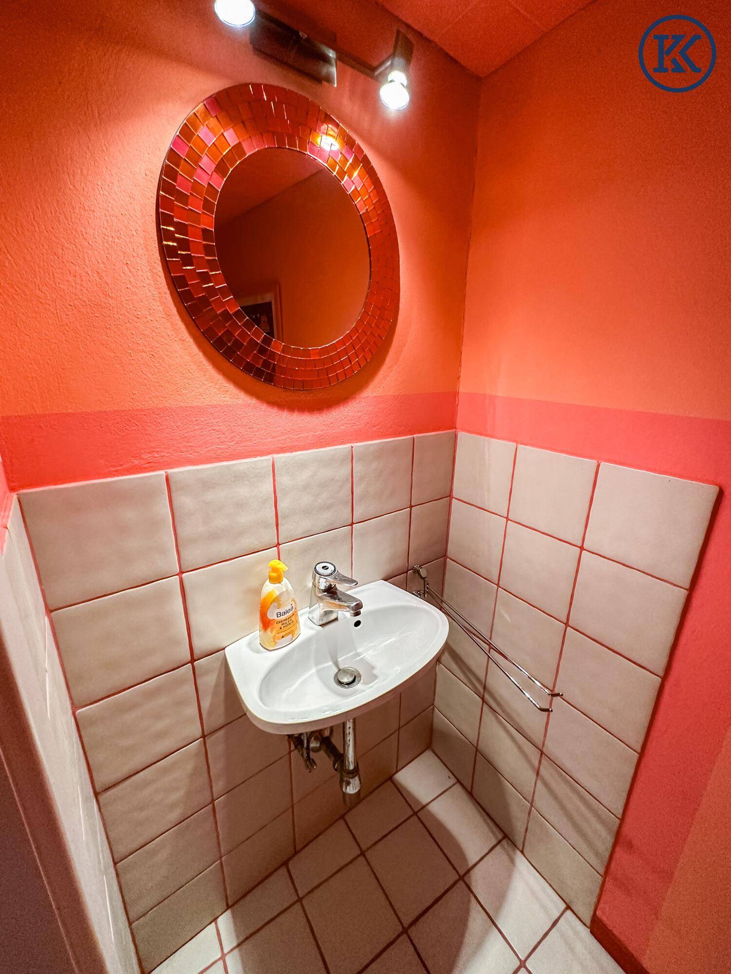 Kleines WC mit Einzelwaschbecken, rundem Spiegel und rosa Wänden, funktional und hell.