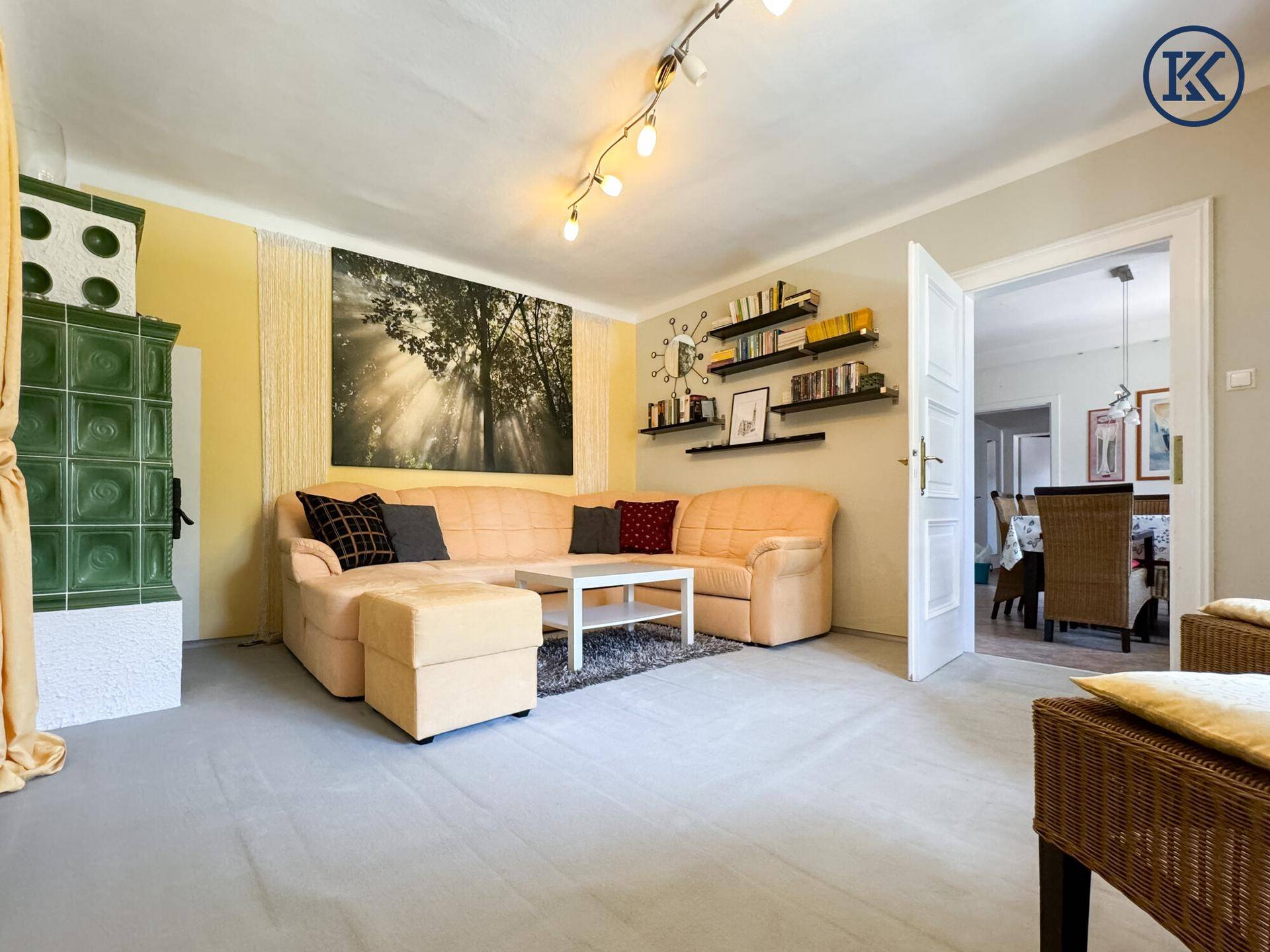 Wohnzimmer mit beigem Sofa, Kachelofen und offenem Zugang zu einem angrenzenden Essbereich.