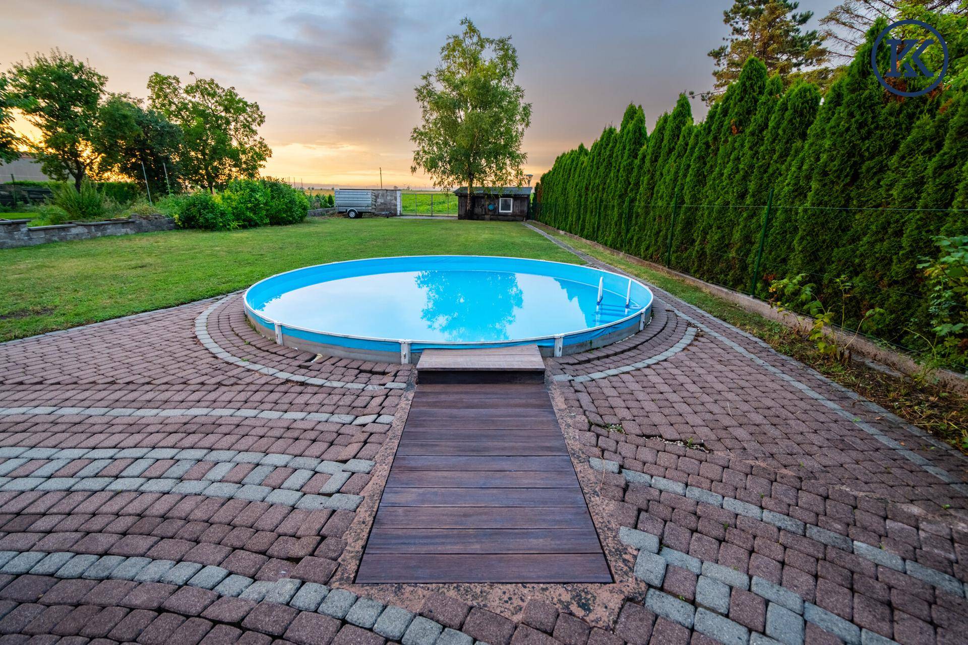 Attraktiver Gartenbereich mit einem oberirdischen Pool und gepflasterter Terrasse bei Sonnenuntergang.