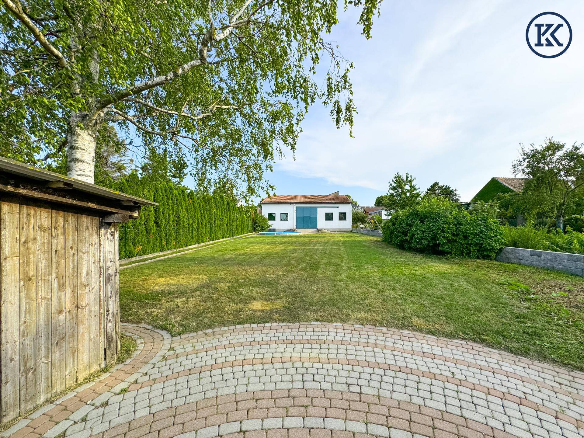 Großer Rasenbereich im Garten mit einem Holzschuppen und Blick auf ein Gebäude im Hintergrund.