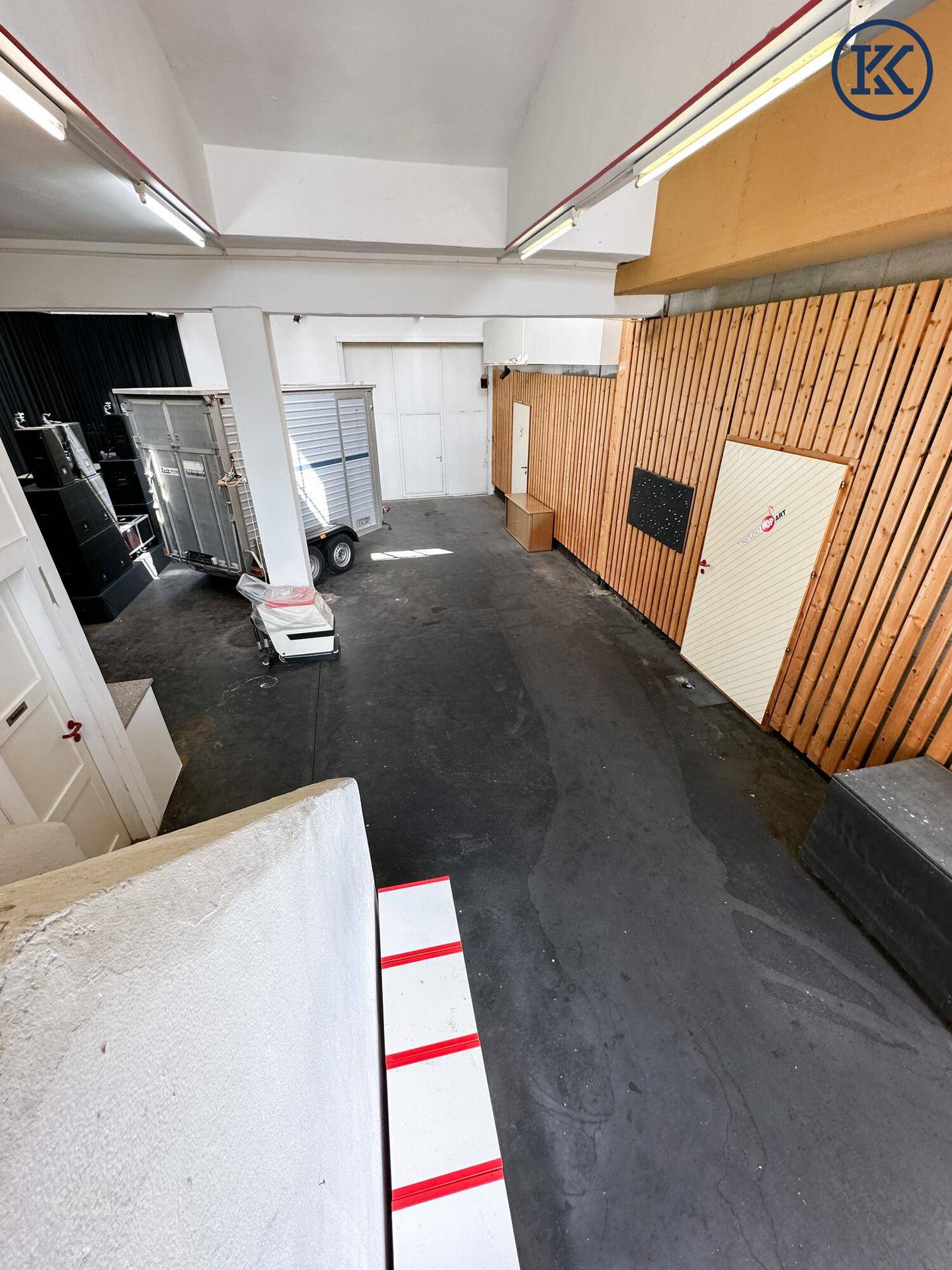 Großer offener Raum mit Betonboden, Holzverkleidung an der Wand und einem Anhänger.