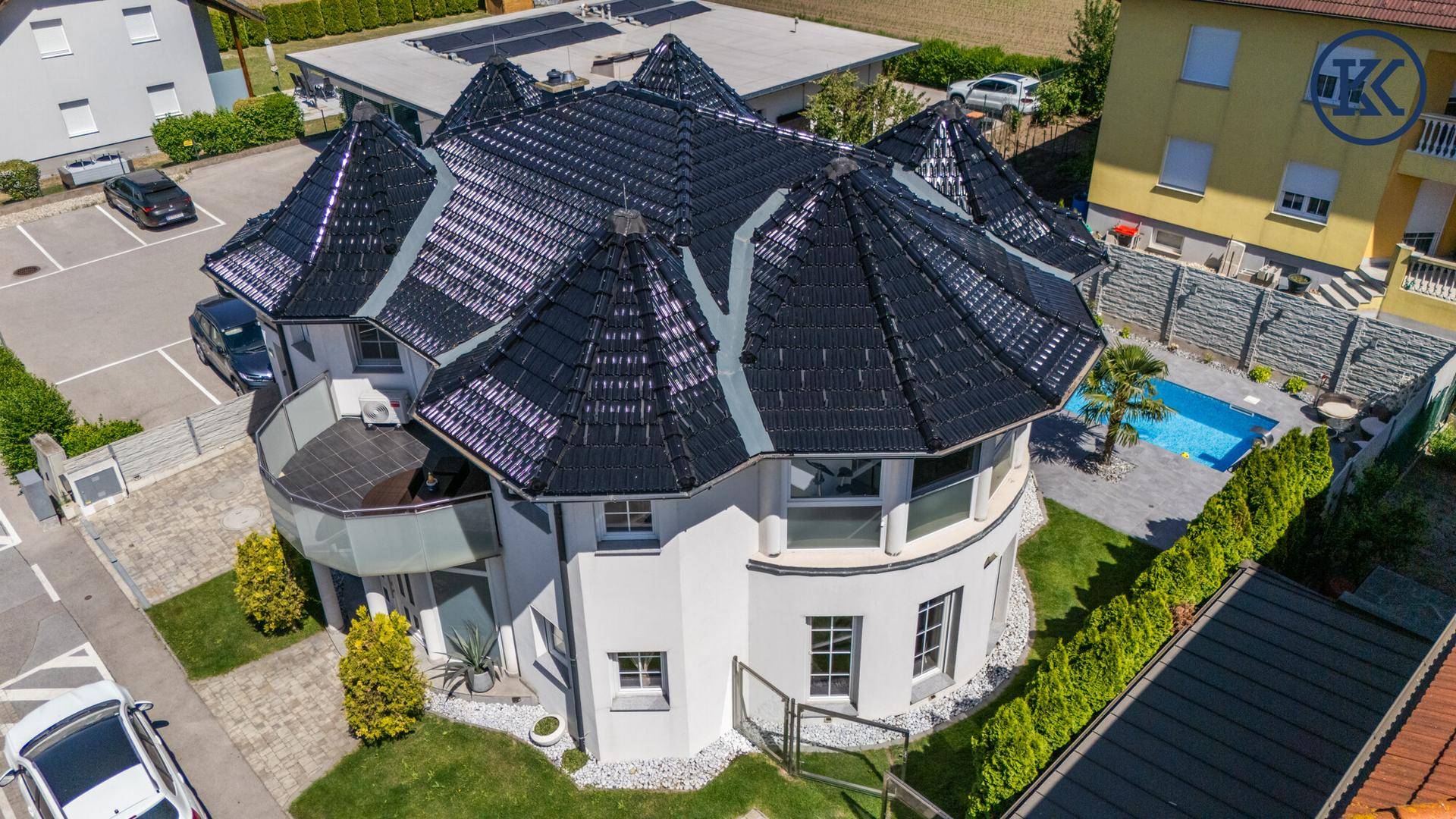 Seitenansicht des Hauses von oben mit geschwungener Fassade, Pool und Garten.