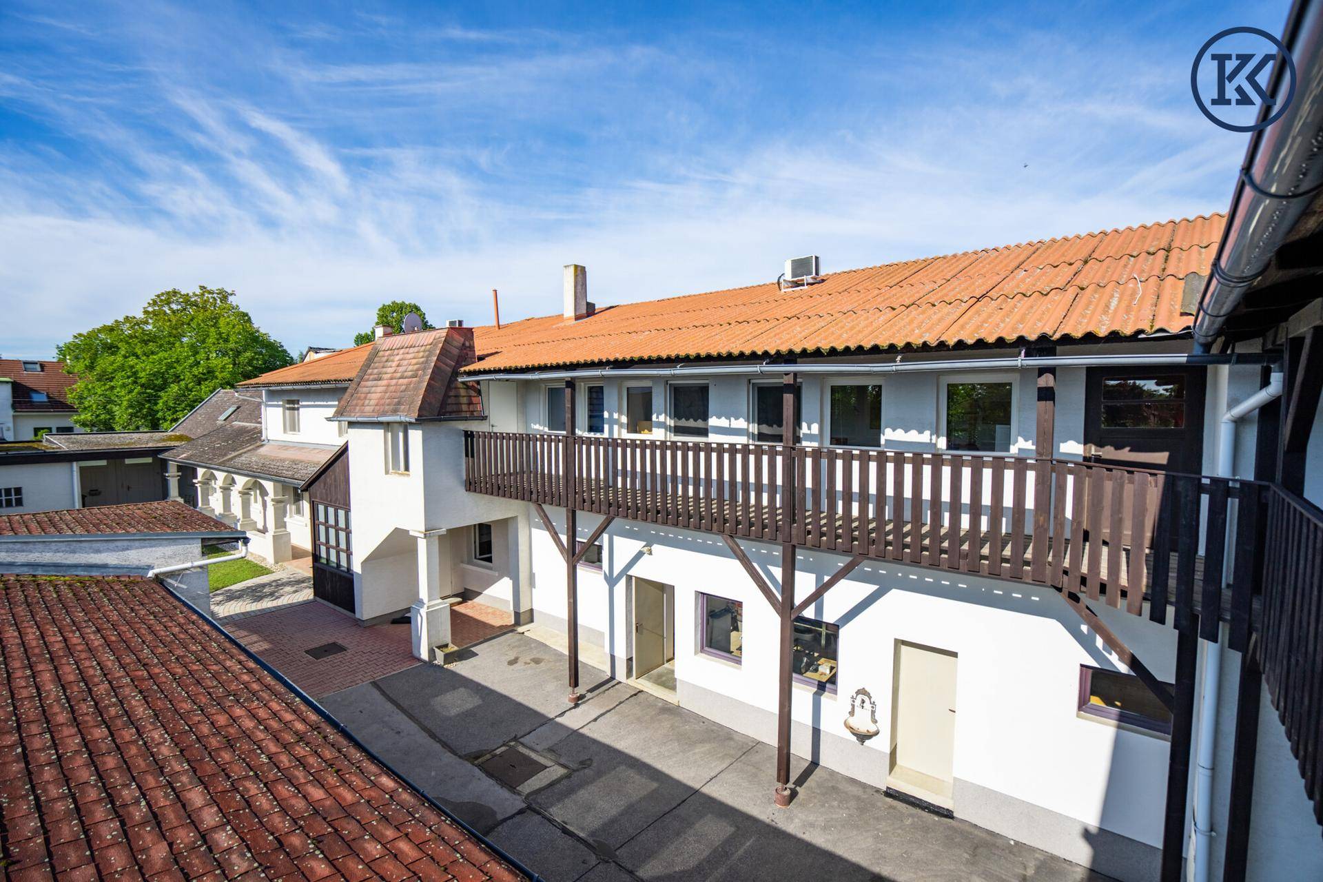 Blick auf die weiße Fassade des Gebäudes mit Holzbalkon und gepflastertem Innenhof.