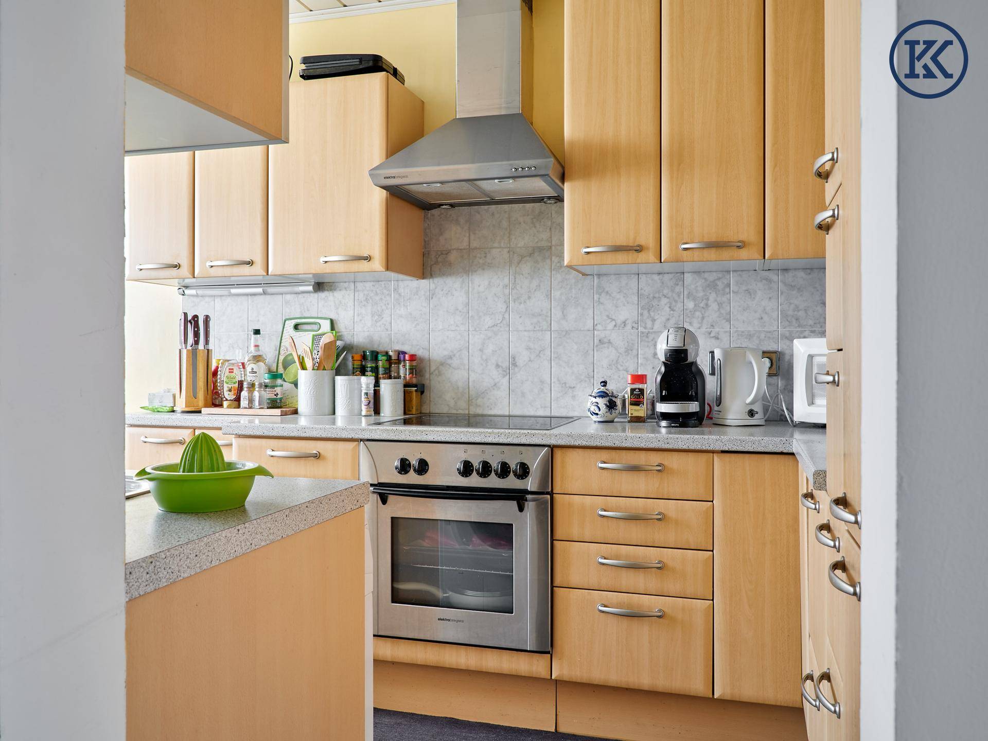 Funktionale Küche mit hellen Holzfronten, Backofen und Dunstabzugshaube.