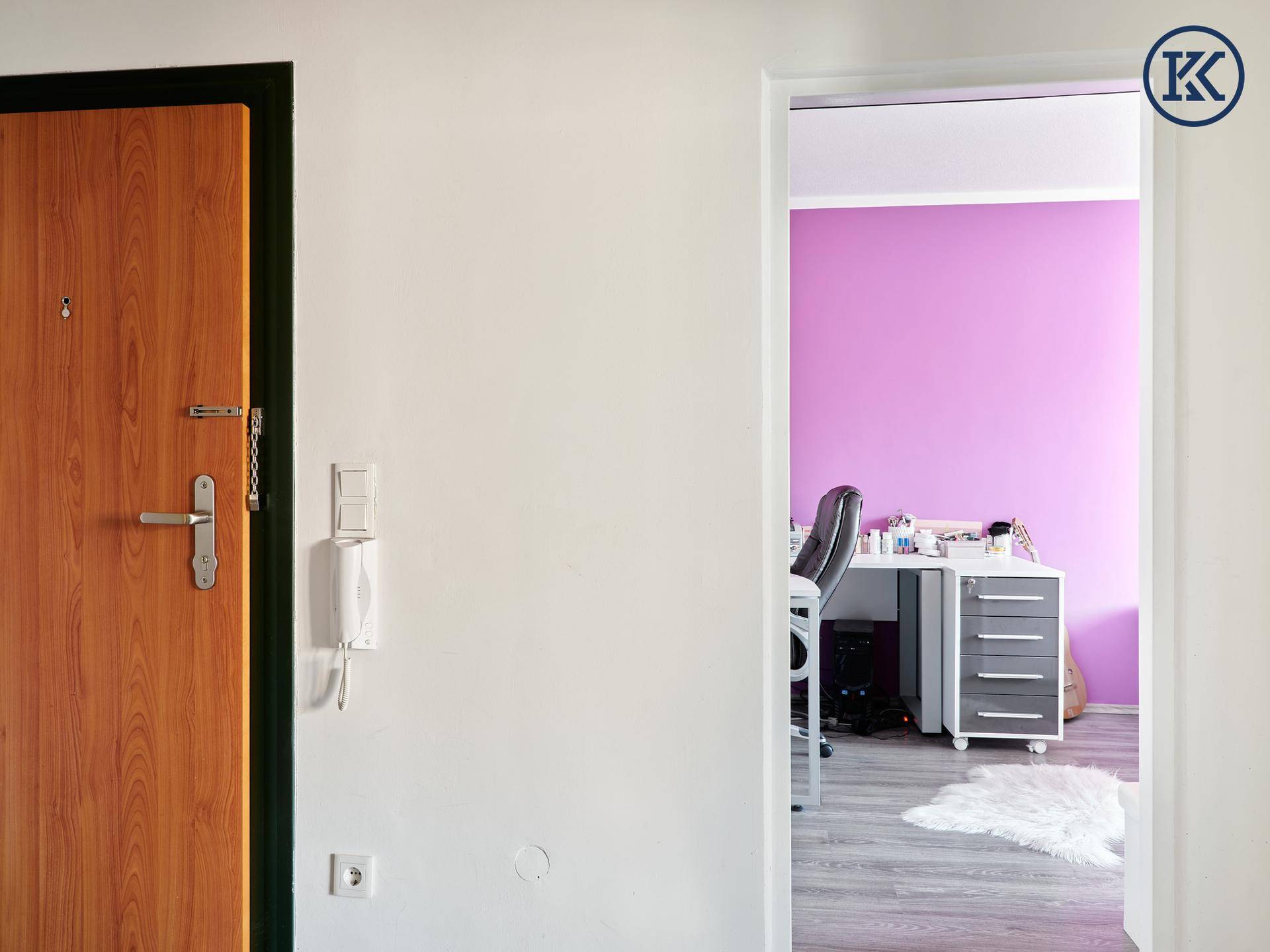 Eingangsbereich mit Holztür und Blick in ein Zimmer mit lila Wand.