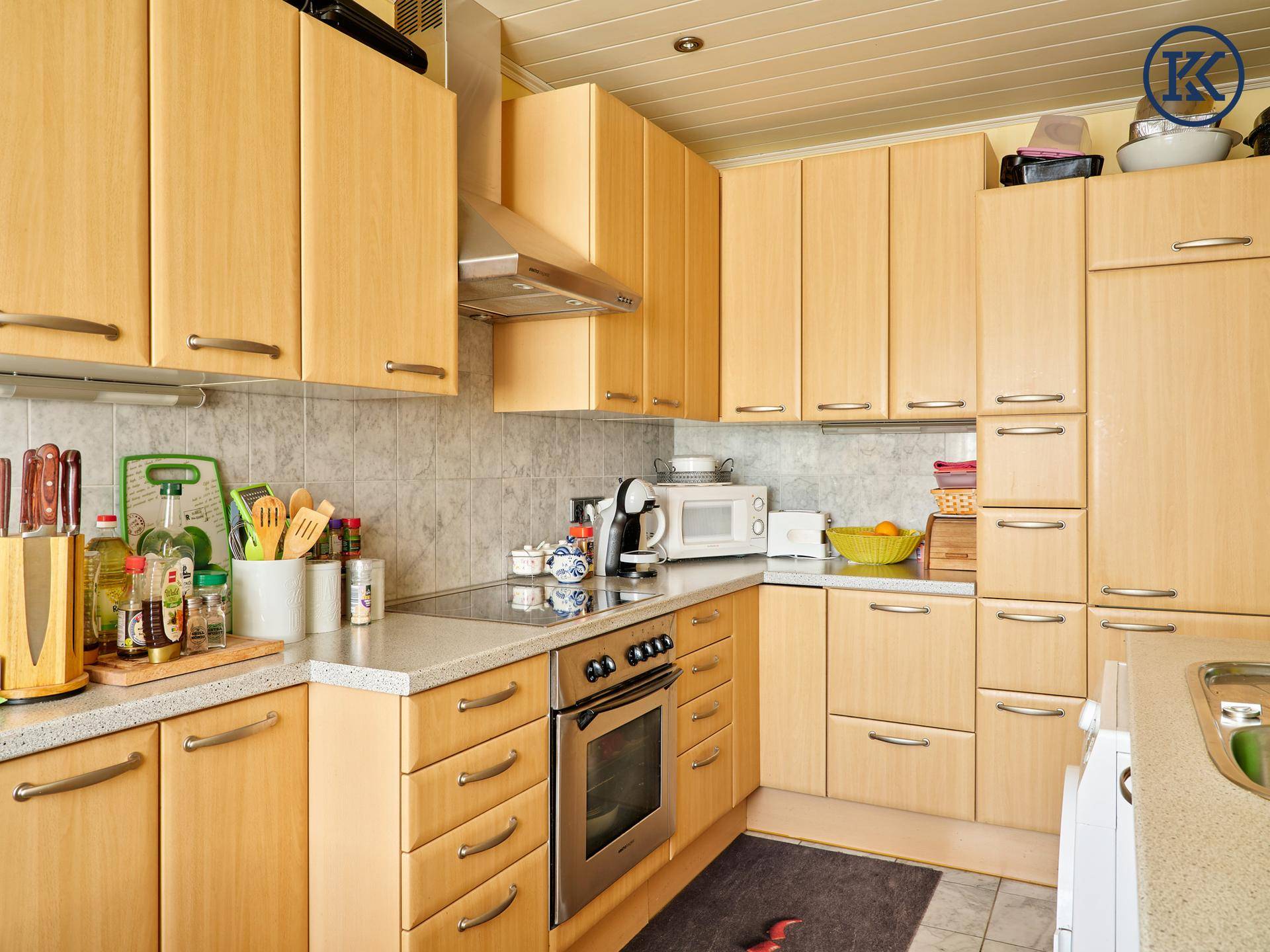 Geräumige Küche mit vielen Holzschränken, Kochfeld und Mikrowelle.