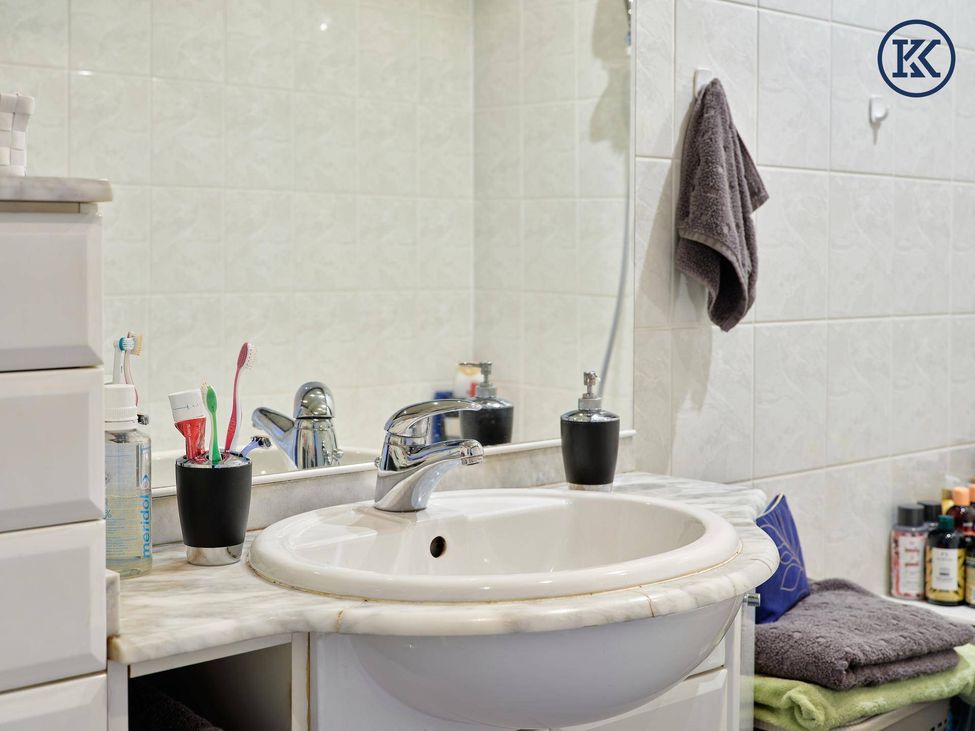 Waschbecken im Badezimmer mit großem Spiegel und Fliesen an den Wänden.