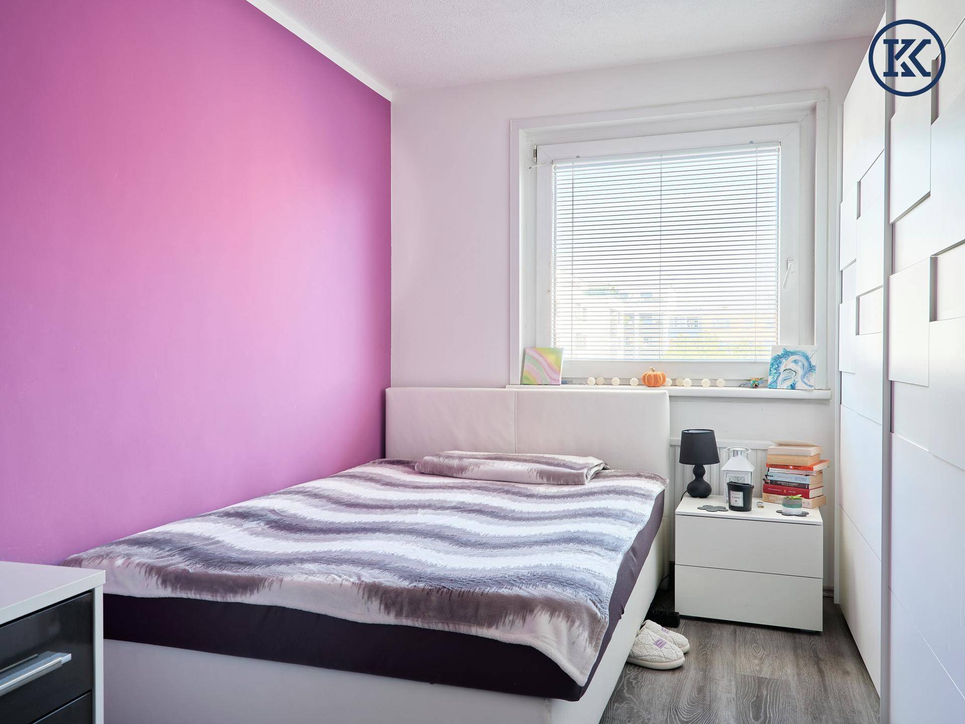 Helles Schlafzimmer mit Bett, Nachttisch und Fenster mit Jalousien.