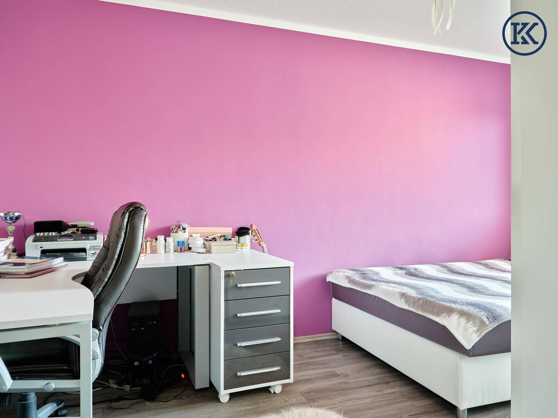 Schlafzimmer mit lila Wand, Schreibtisch und Bett mit gestreifter Decke.