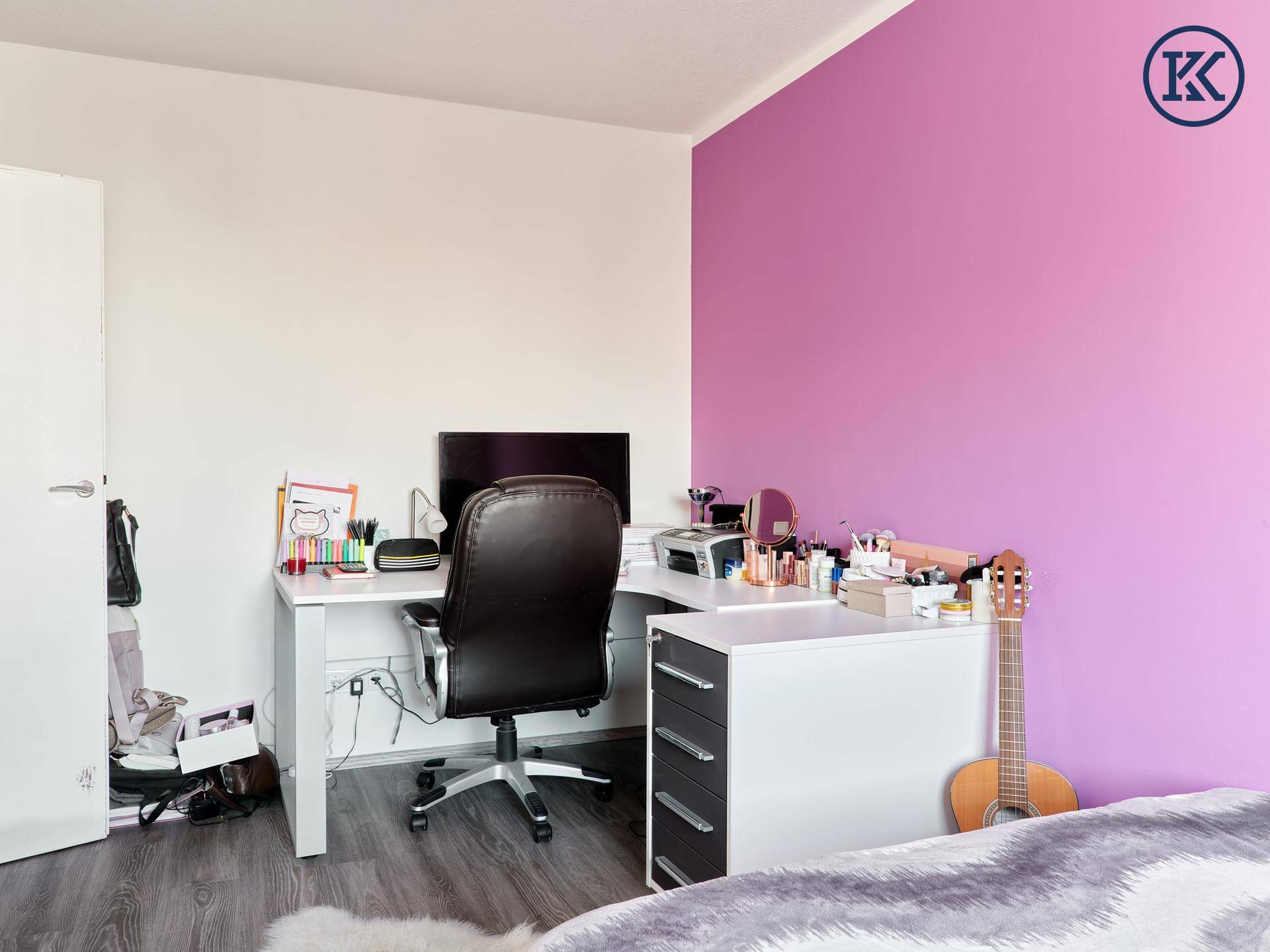 Schlafzimmer mit Schreibtisch, Computer und Bett mit lila Wandakzent.