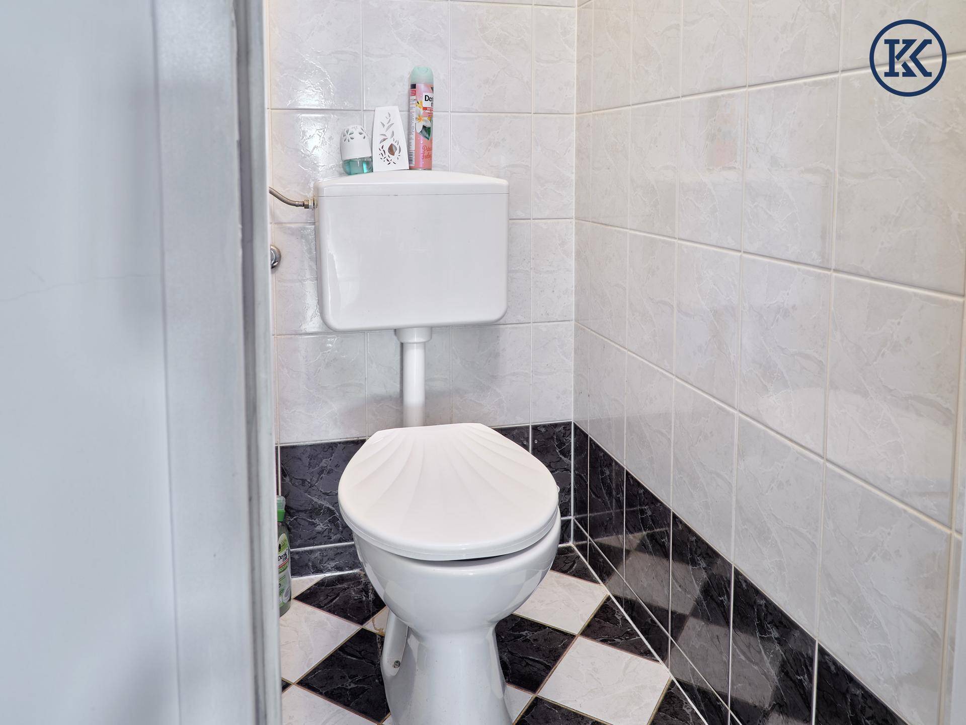 Separate Toilette mit Fliesenboden in Schwarz-Weiß und weißer Keramik.