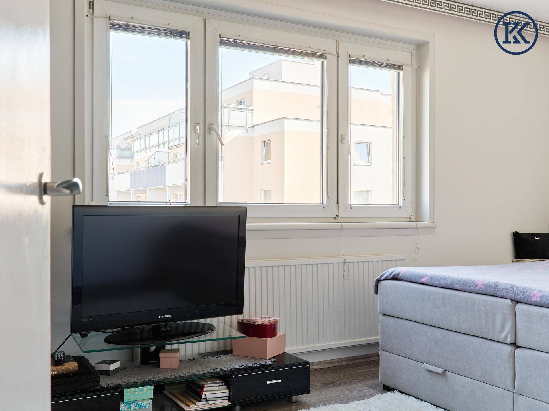 Schlafzimmer mit Fensterfront, die viel Tageslicht hereinlässt, und einem Fernseher auf einem Sideboard.