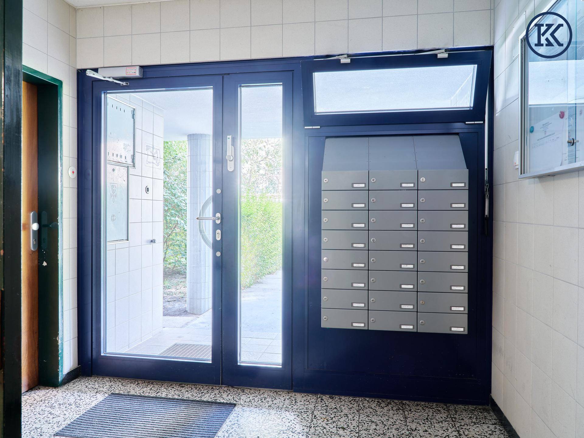 Eingangsbereich eines Mehrfamilienhauses mit Briefkästen und einer großen Glastür.