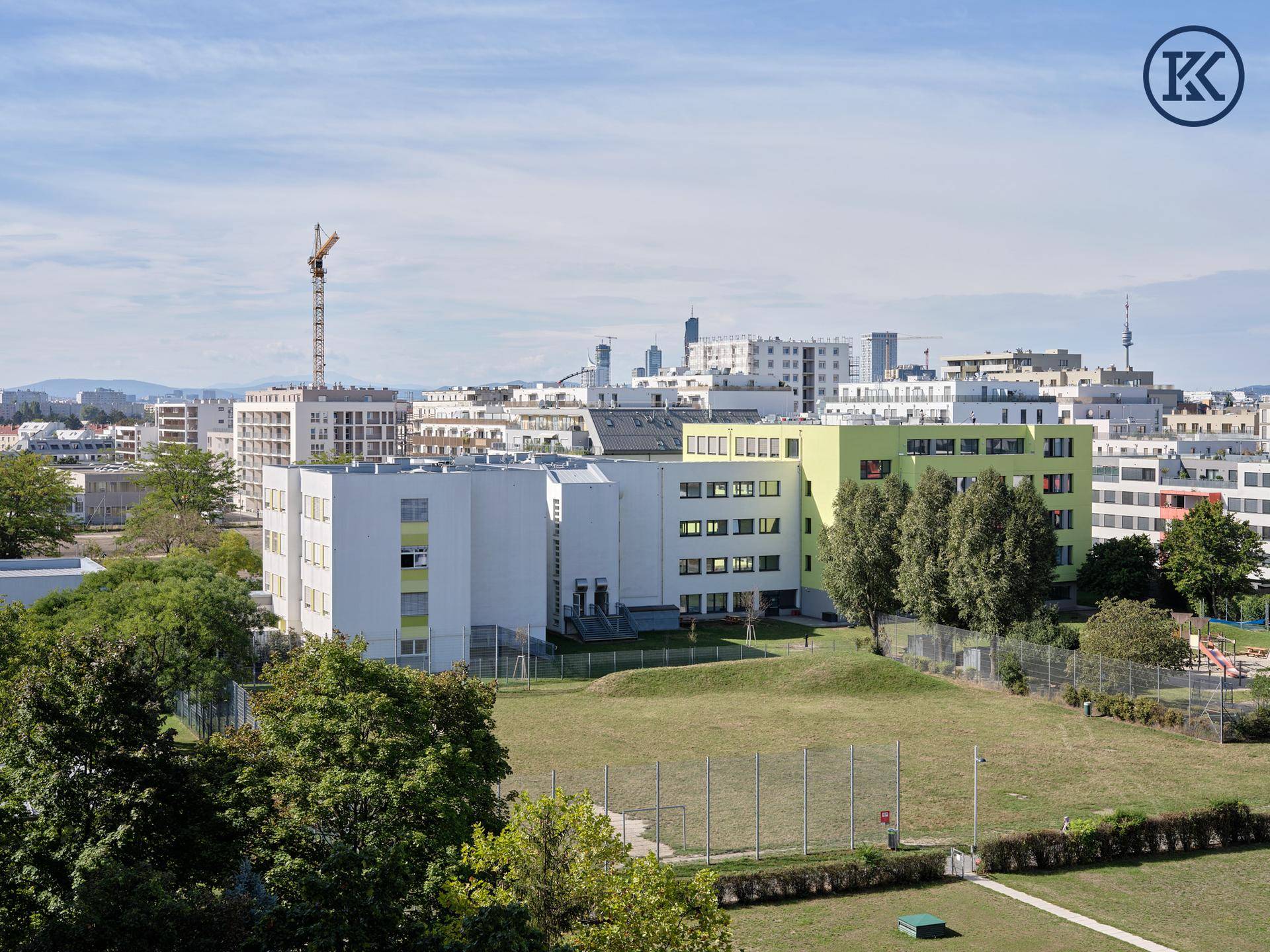 Weitläufige Ansicht von Wohngebäuden und einer großen Grünfläche unter blauem Himmel.
