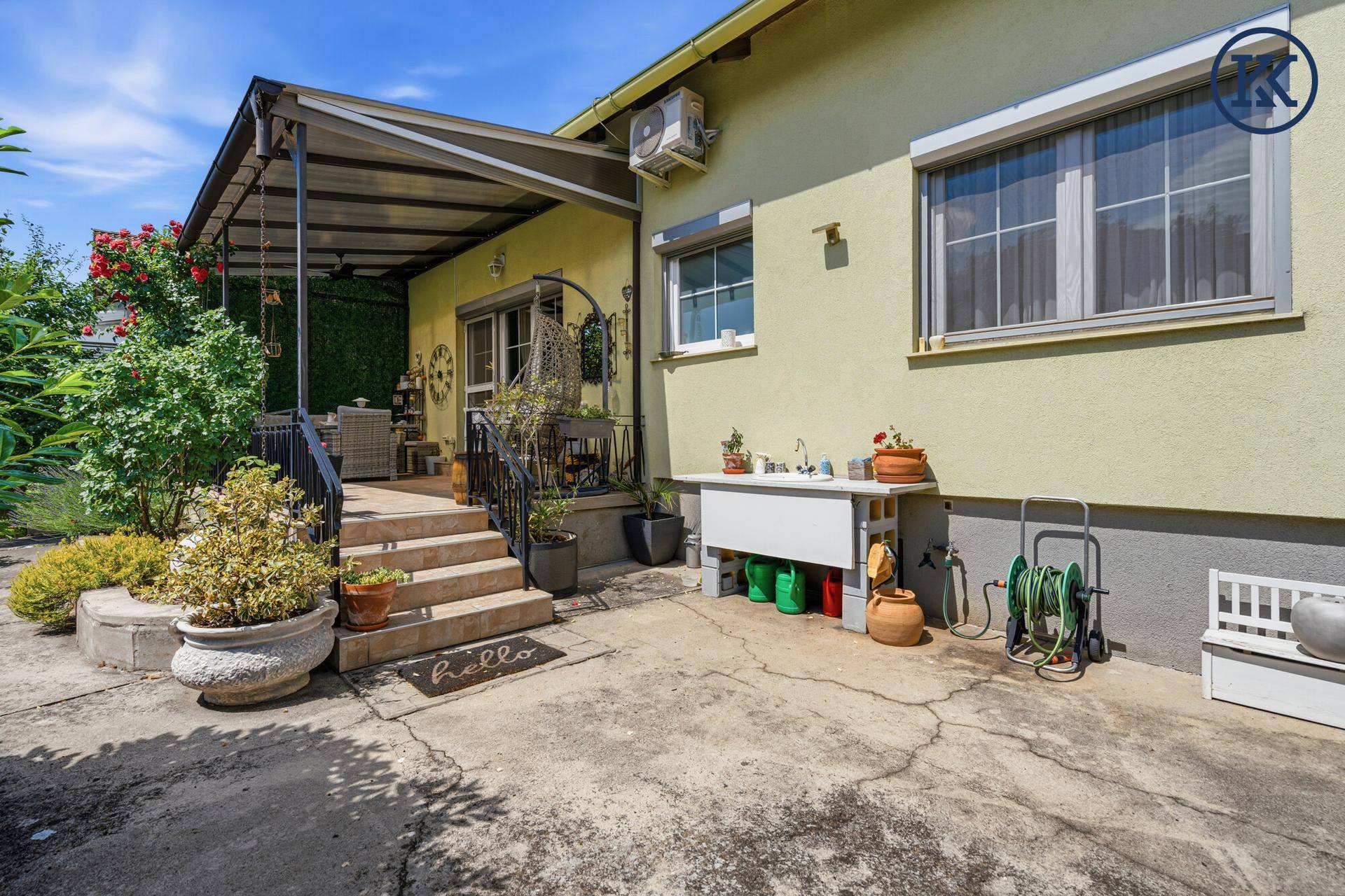 Gepflasterter Bereich vor dem Haus mit Außenspüle und Zugang zur überdachten Terrasse.