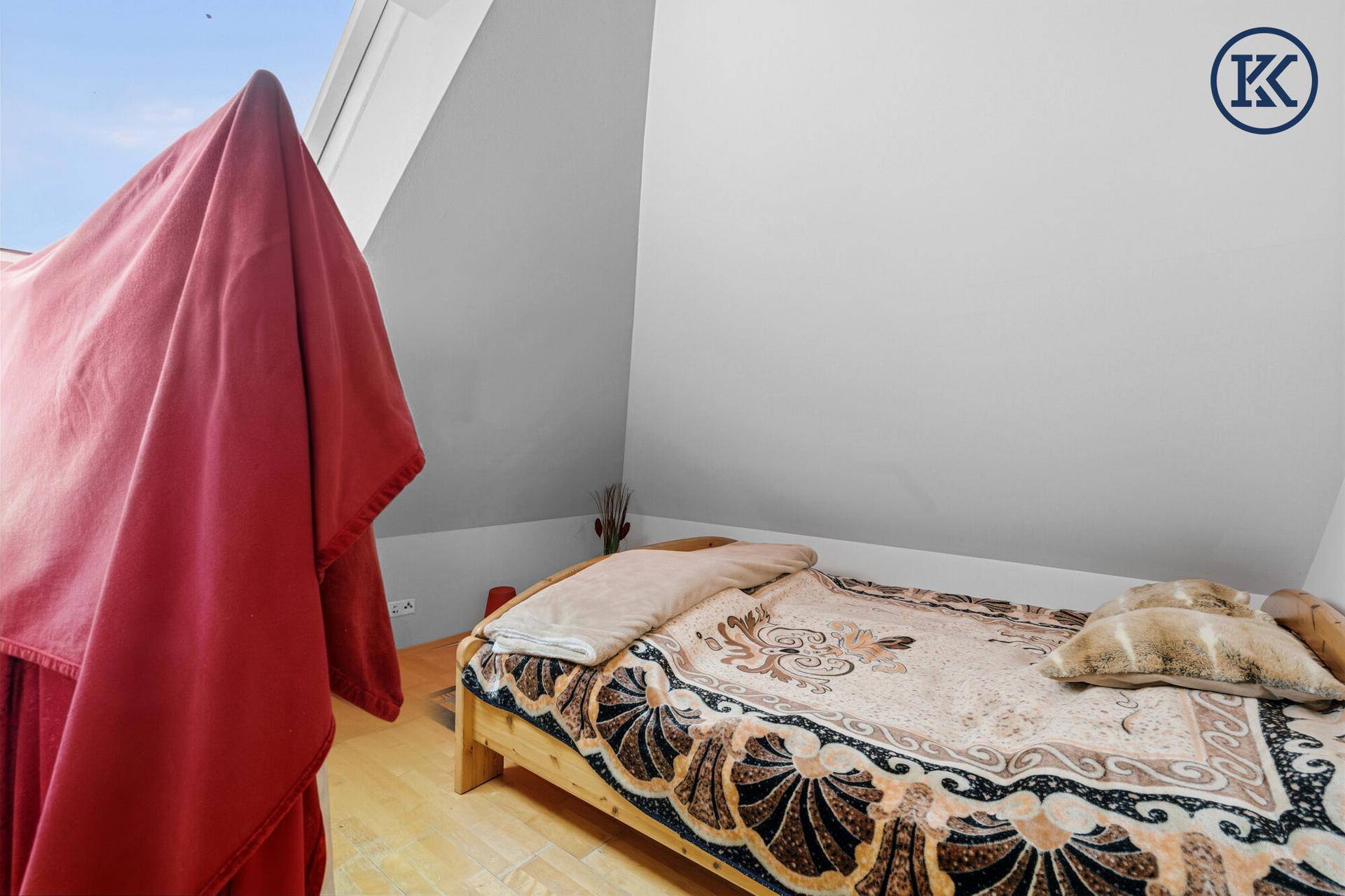 Gemütliches Schlafzimmer im Dachgeschoss mit schräger Decke, Holzbett und Dachfenster.