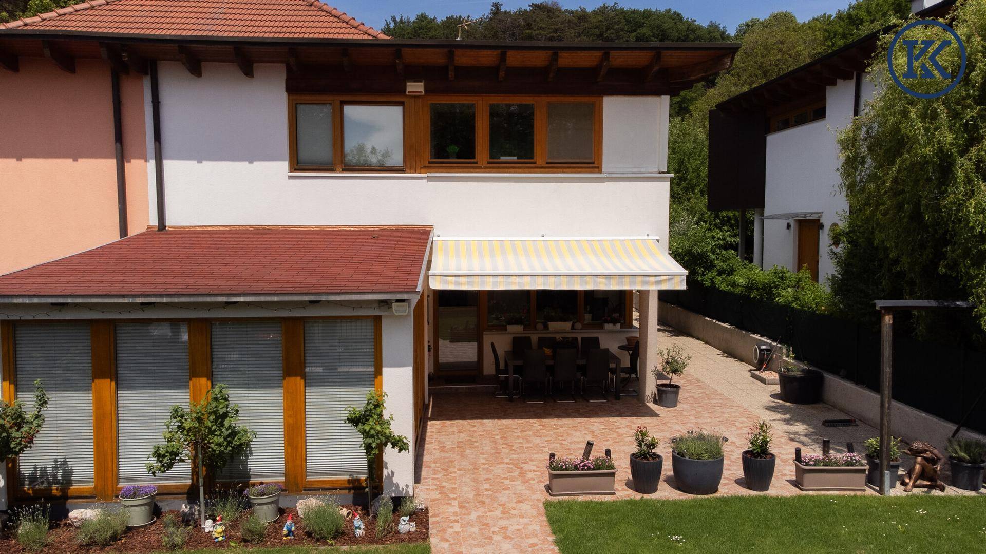 Gepflegter Gartenbereich mit großer Terrasse, Markise und Wintergarten, umgeben von Bäumen.