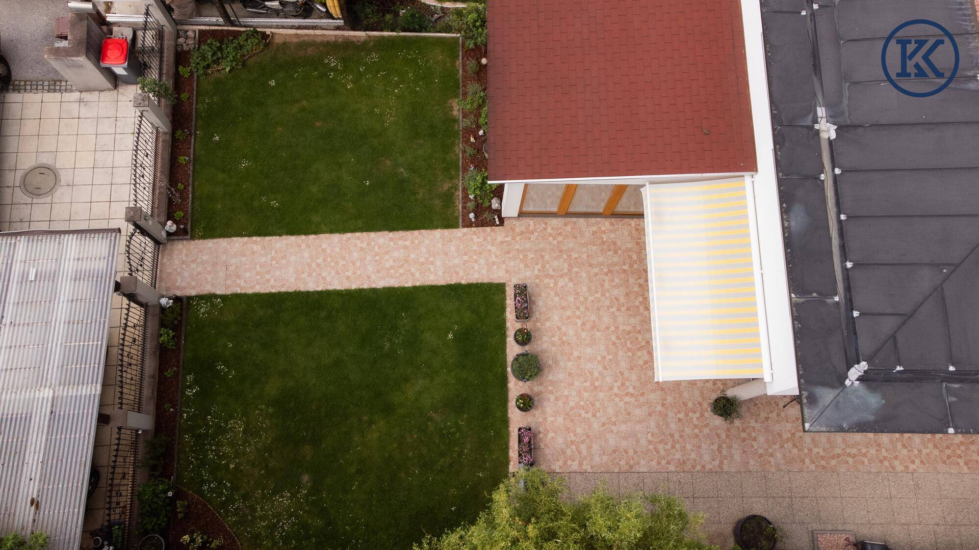 Draufsicht auf den gepflegten Garten mit Rasenflächen, gepflasterten Wegen und einer Markise.