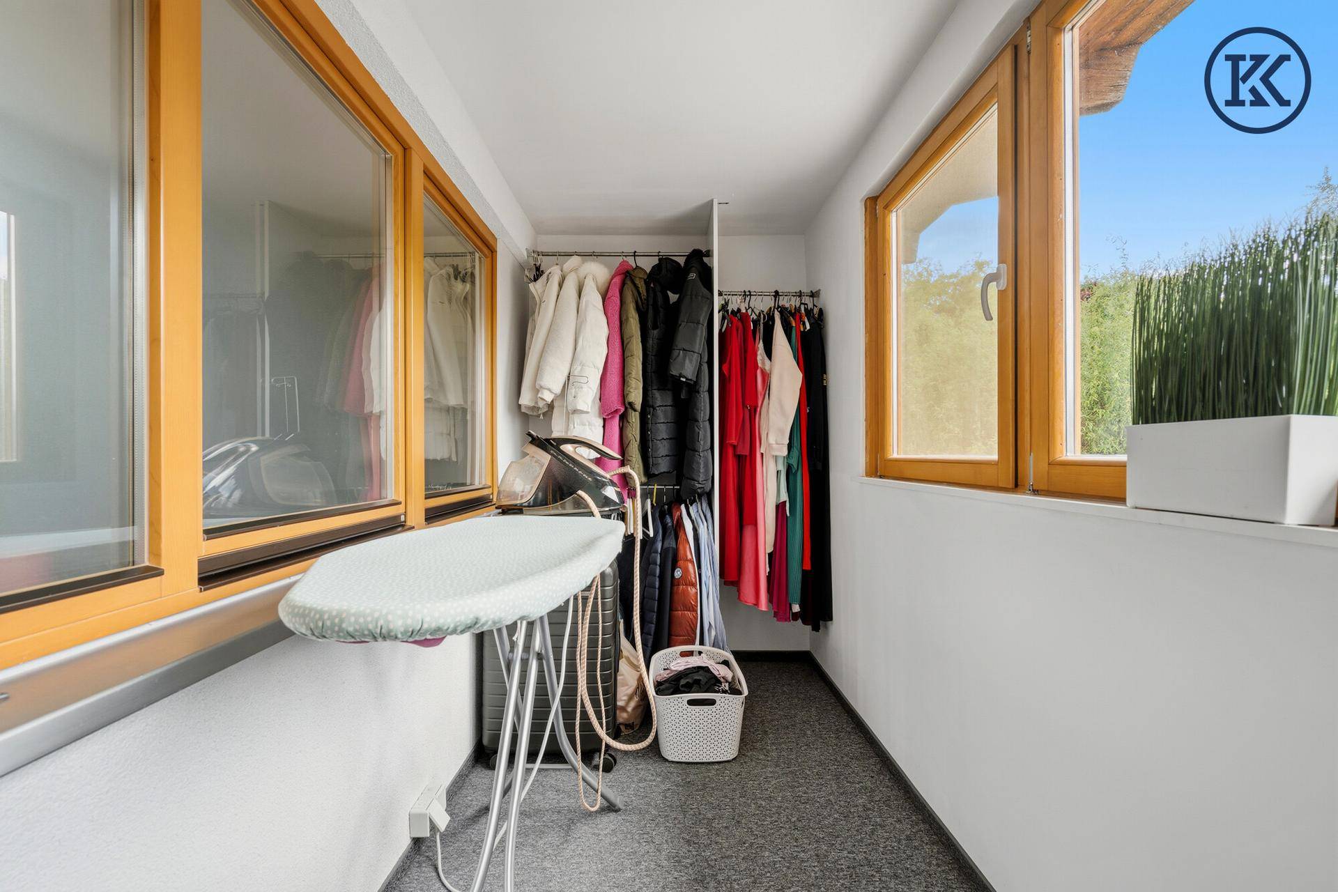 Praktischer Hauswirtschaftsraum mit Kleiderstangen, Bügelbrett und großen Fenstern für Tageslicht.