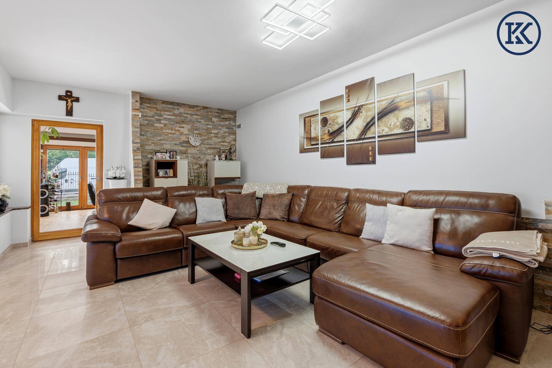 Gemütliches Wohnzimmer mit großem Ledersofa, Fliesenboden und dekorativer Steinwand.