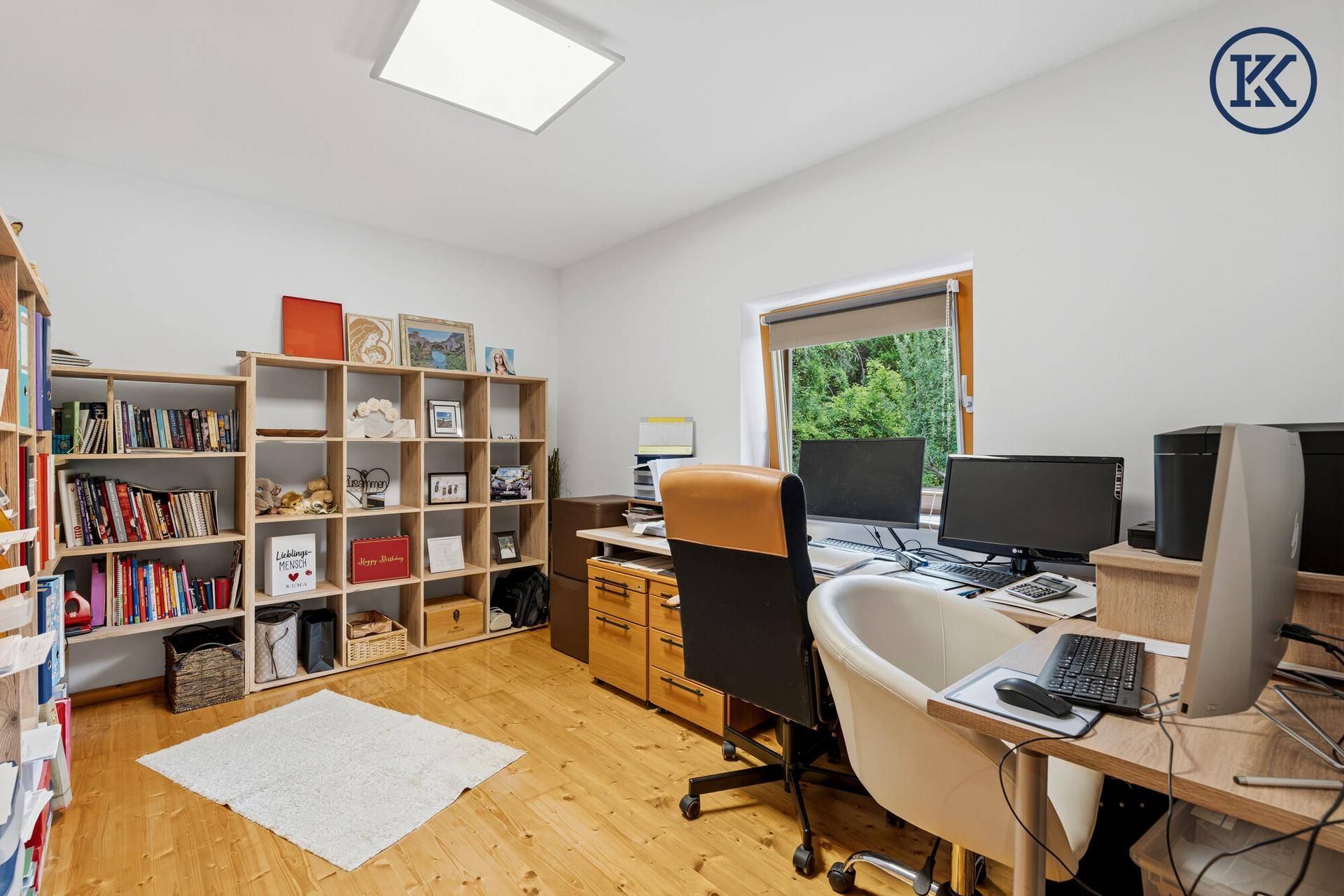 Helles Arbeitszimmer mit Bücherregalen, zwei Schreibtischen und Blick ins Grüne.