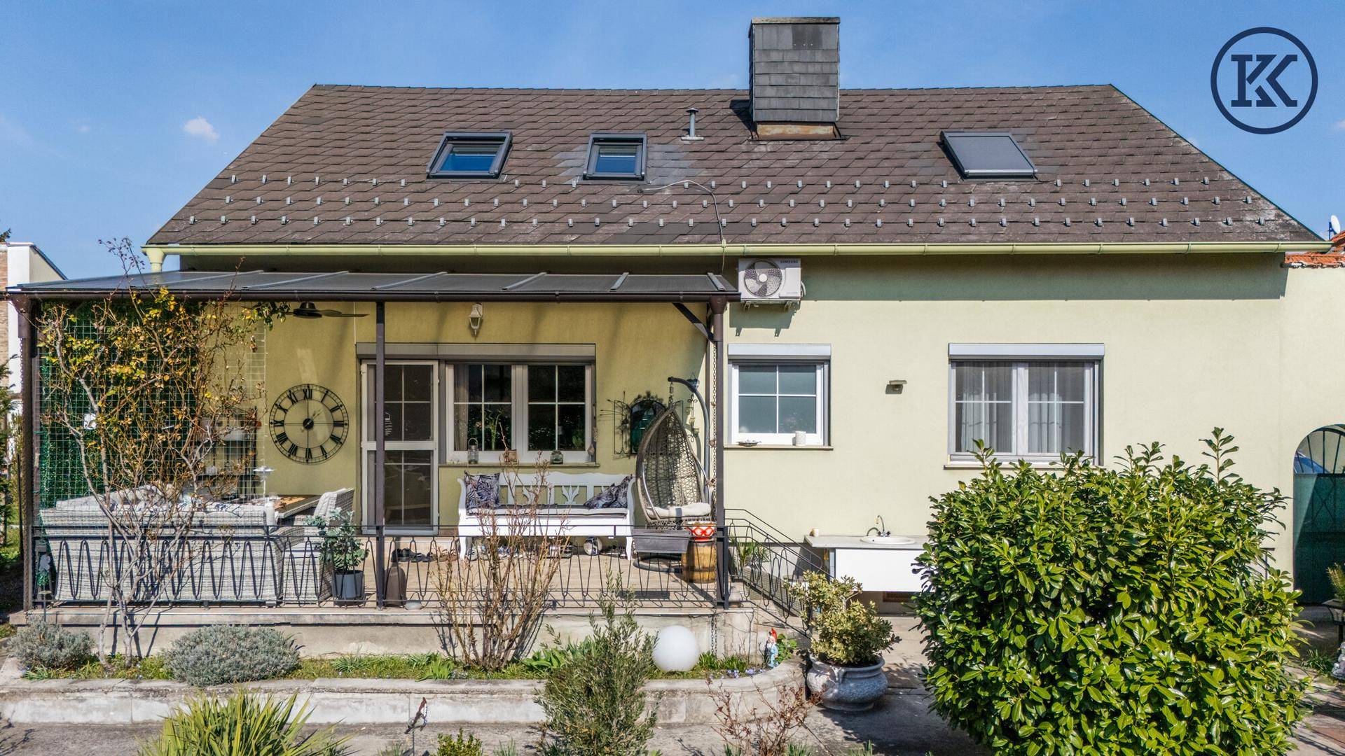 Rückseite des Hauses mit überdachter Terrasse, Sitzgelegenheiten und Gartenblick.
