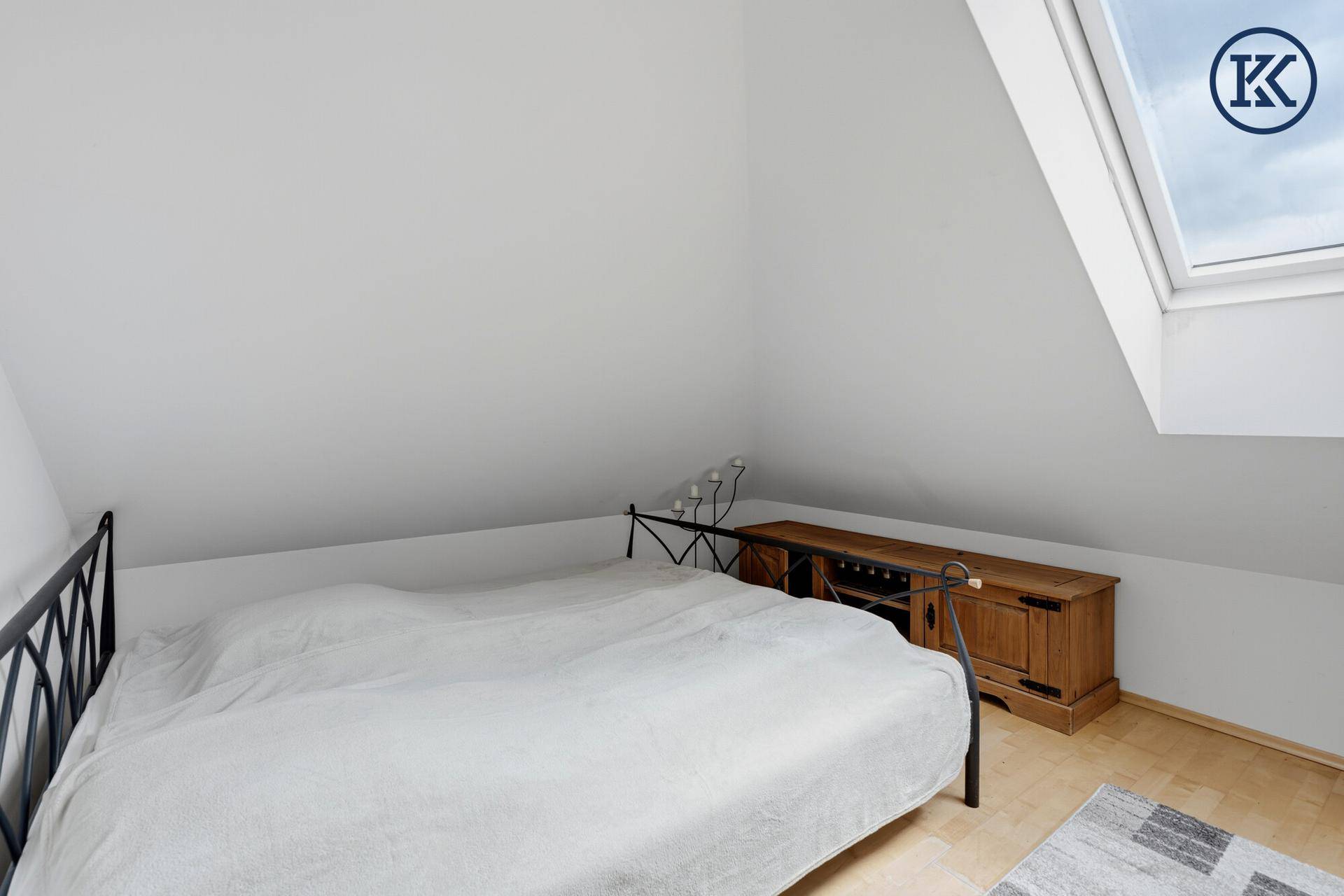 Helles Schlafzimmer im Dachgeschoss mit Holzboden und Dachfenster.