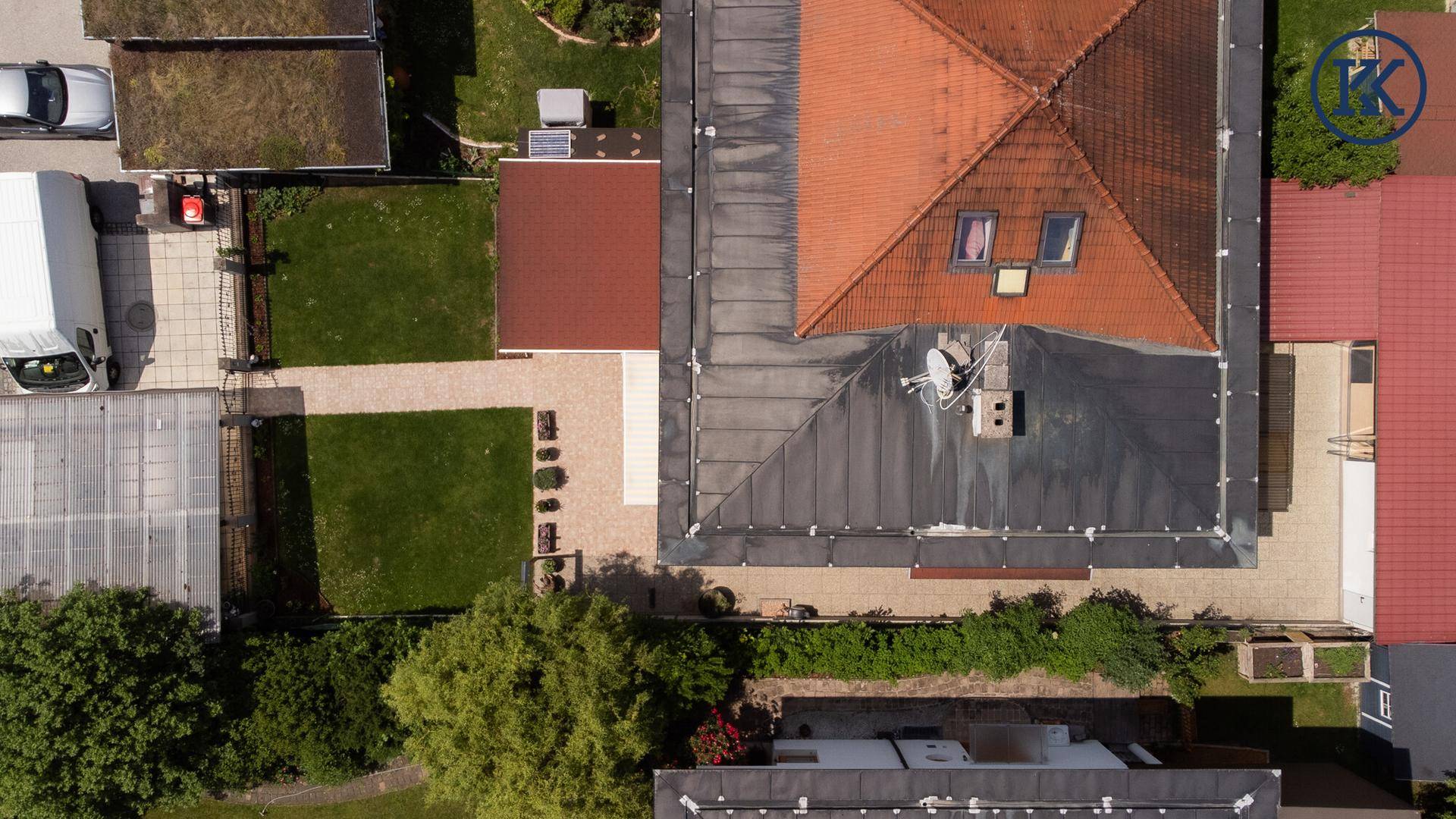 Draufsicht auf das Hausdach mit Ziegeln und Metallverkleidung sowie den Gartenbereich.