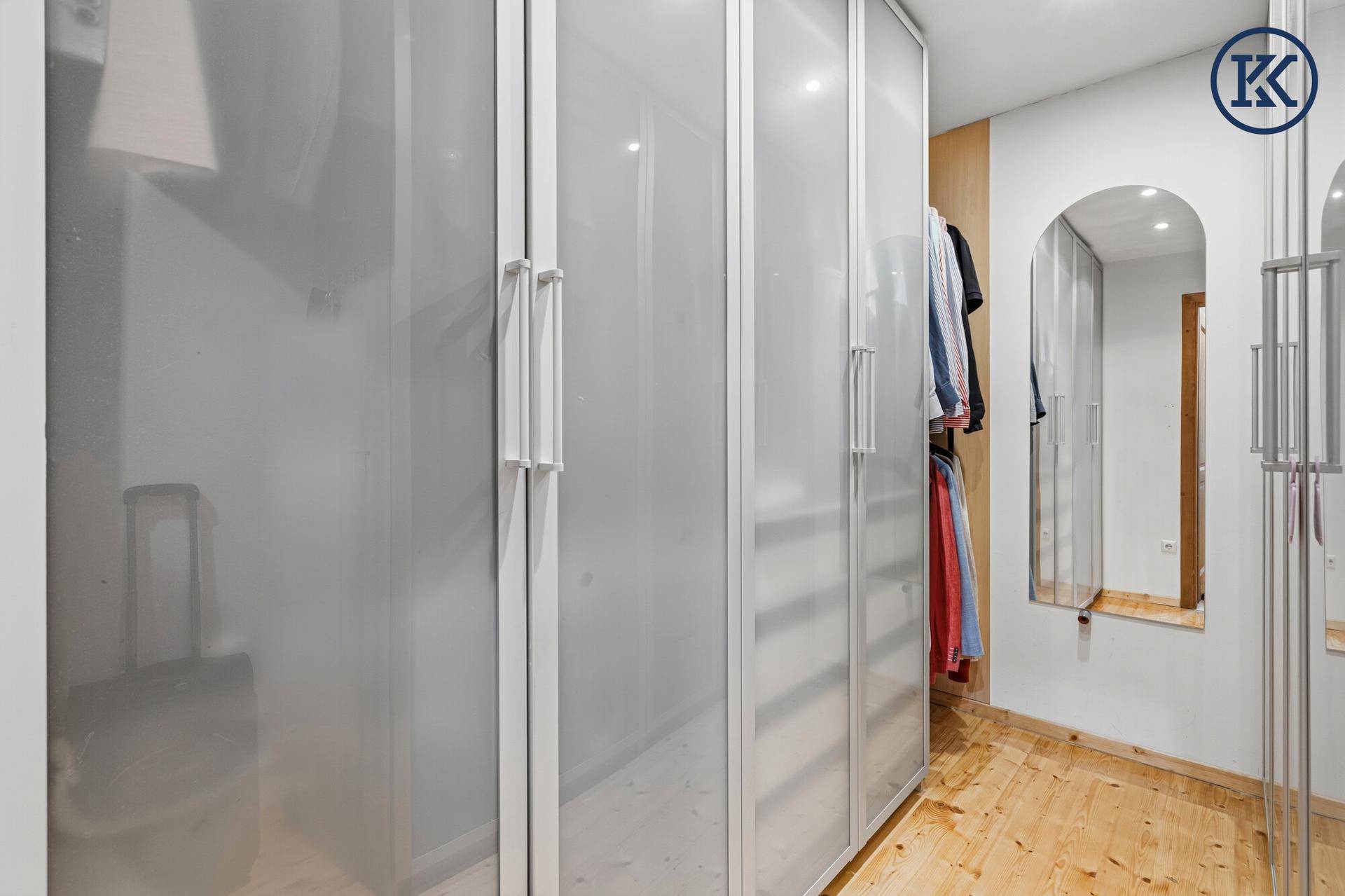 Geräumiger begehbarer Kleiderschrank mit Spiegeltür und Holzboden.