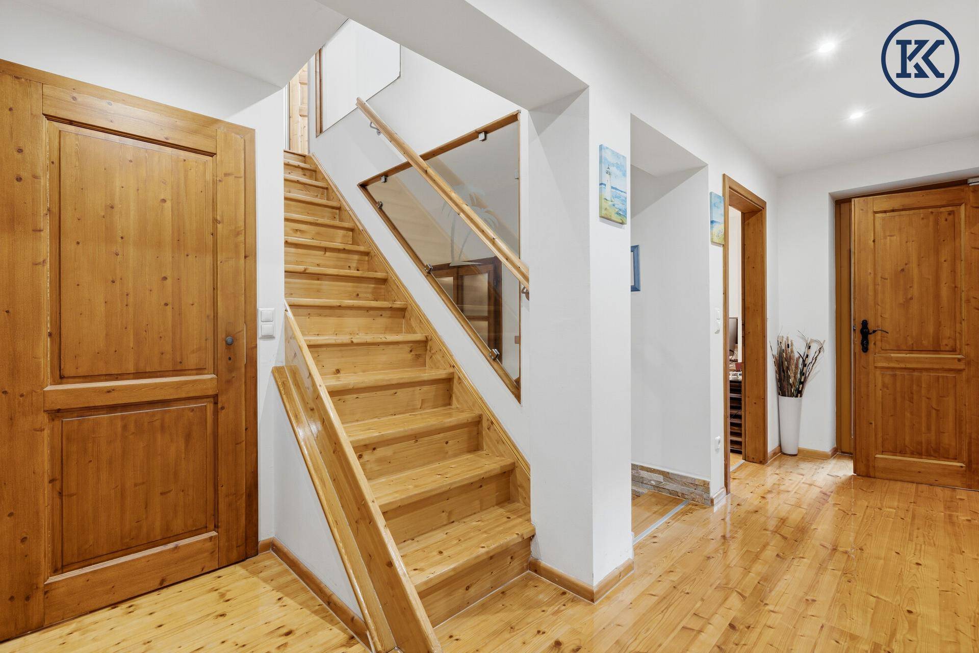 Heller Flur mit Holztreppe, Glasgeländer und Holzboden.