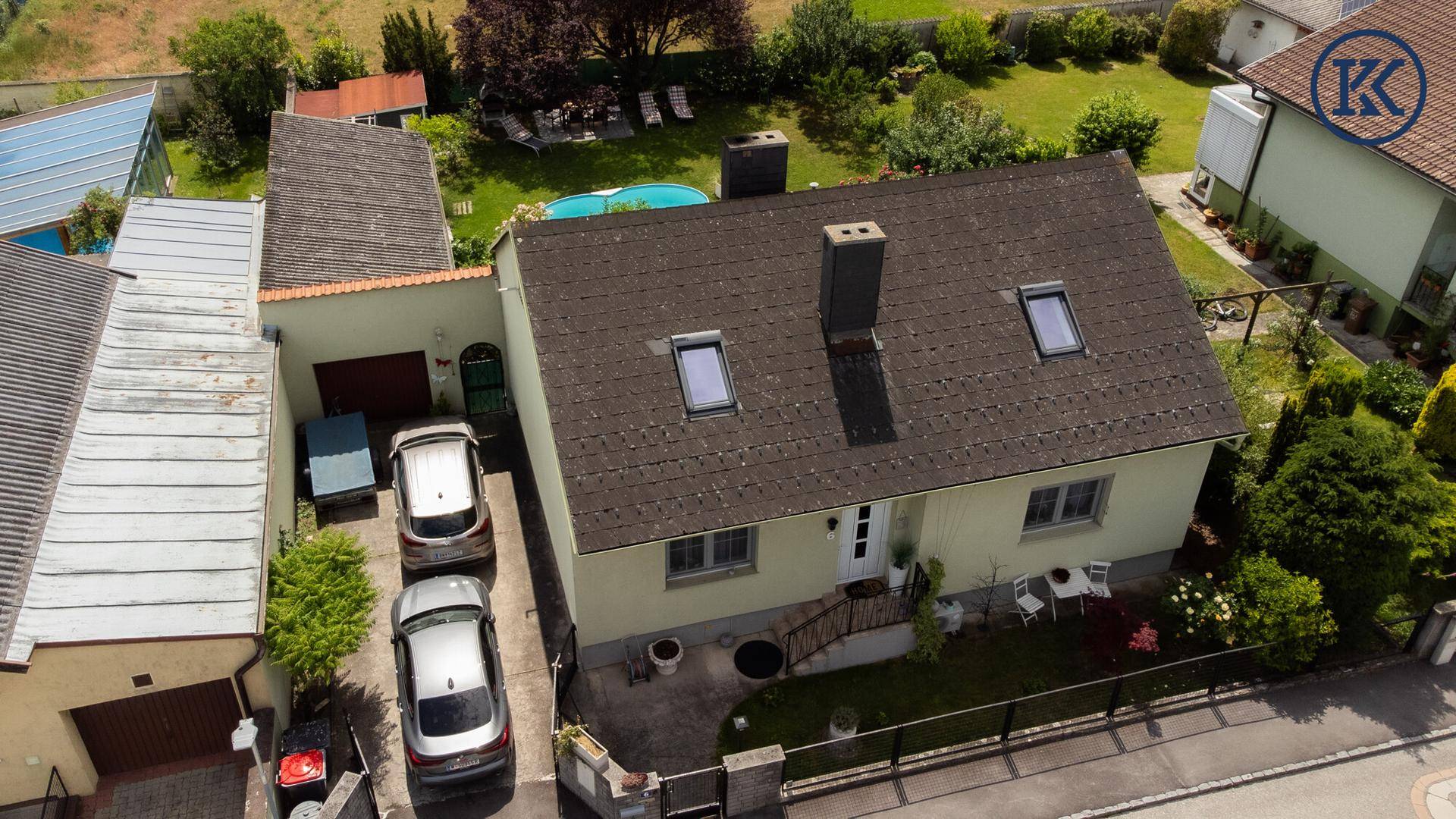 Vorderansicht des Hauses von oben mit Einfahrt, geparkten Autos und dem Eingangsbereich.