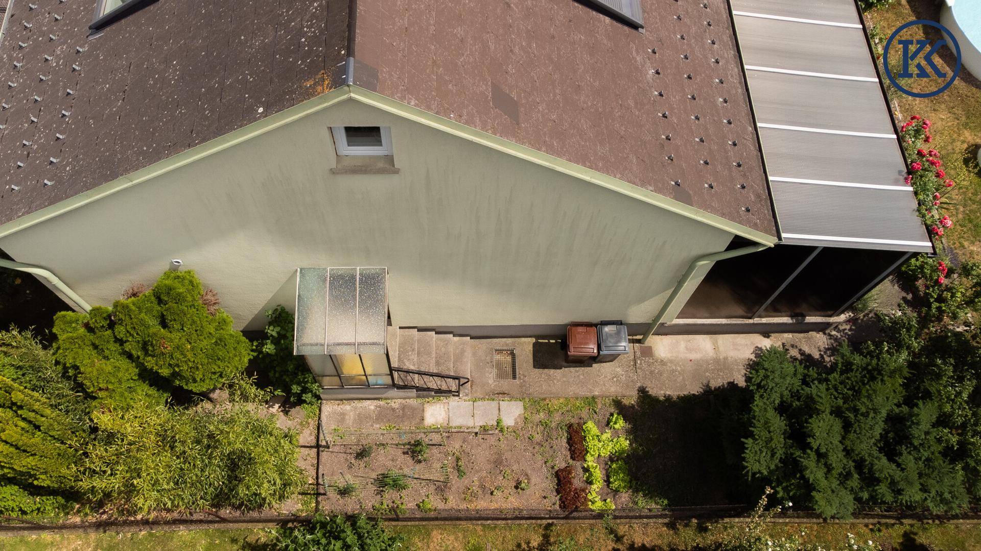 Draufsicht auf die Hausseite mit kleinem Gewächshaus, Treppe und angelegten Gartenbeeten.