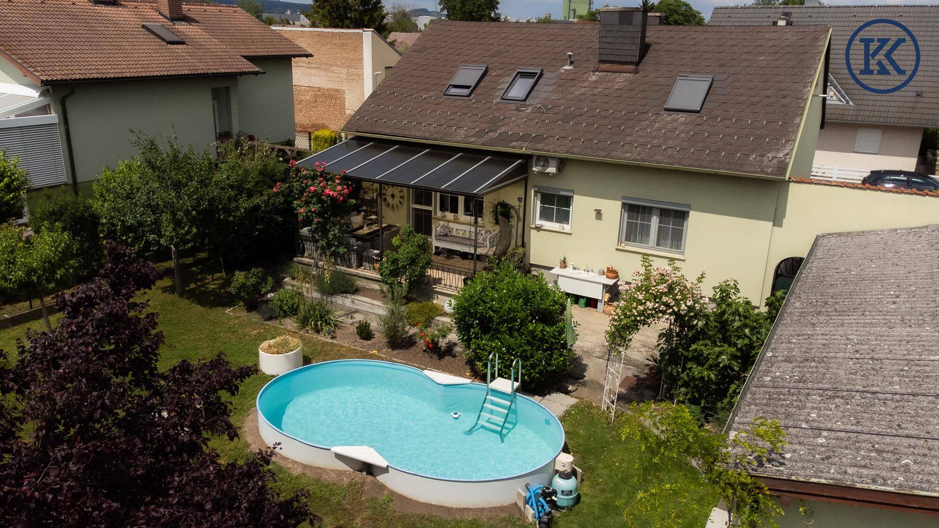 Luftaufnahme des Hauses mit gepflegtem Garten, Pool und überdachter Terrasse, umgeben von Natur.