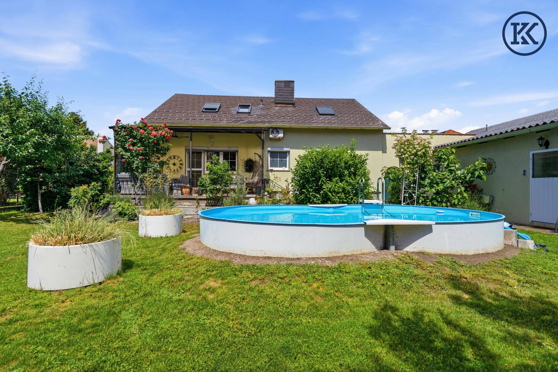 Gepflegter Garten mit ovalem Pool und dem Wohnhaus im Hintergrund an einem sonnigen Tag.