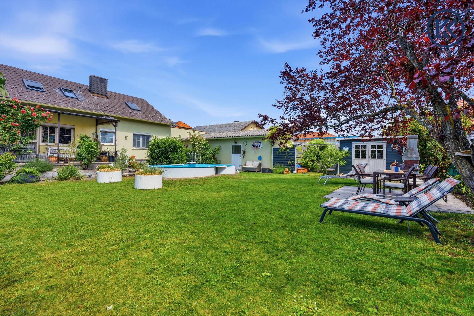 Weitläufiger Garten mit Pool, Essbereich im Freien und dem Wohnhaus im Hintergrund unter blauem Himmel.