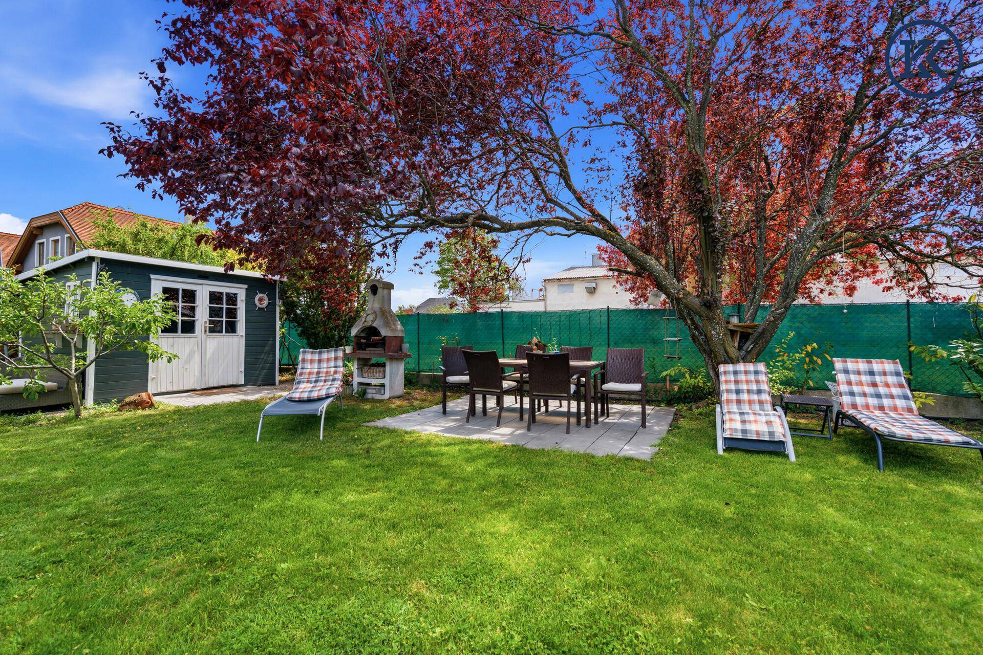 Gartenbereich mit Essplatz im Freien, Gartenhaus, Grill und bequemen Sonnenliegen auf dem Rasen.