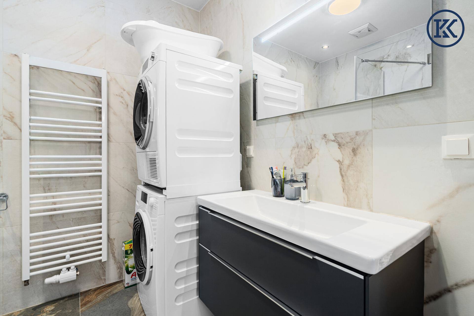 Helles Badezimmer mit Waschbecken, Spiegel und gestapelter Waschmaschine und Trockner.