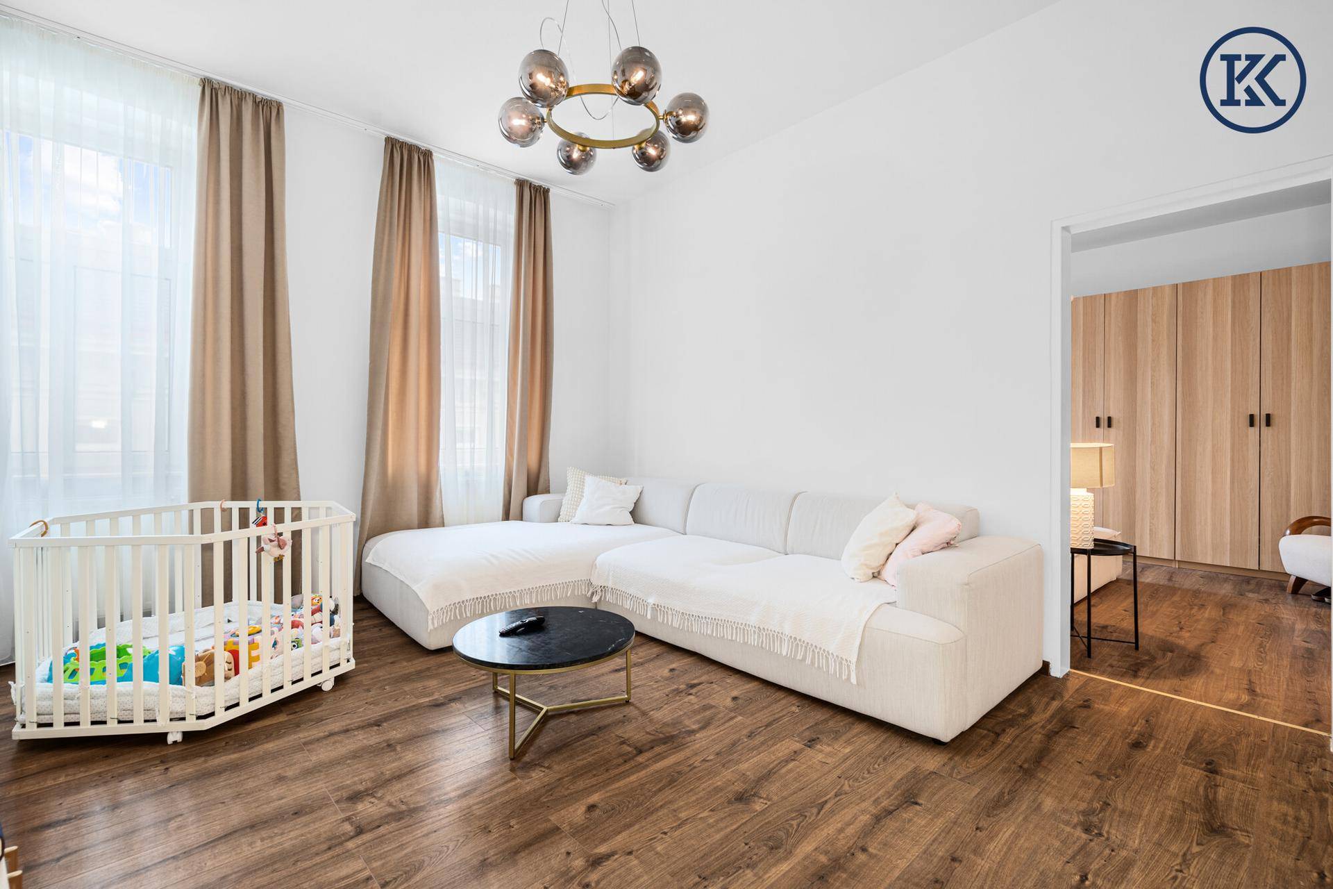 Geräumiges Wohnzimmer mit hellem Sofa, Holzboden und Zugang zu einem weiteren Raum.