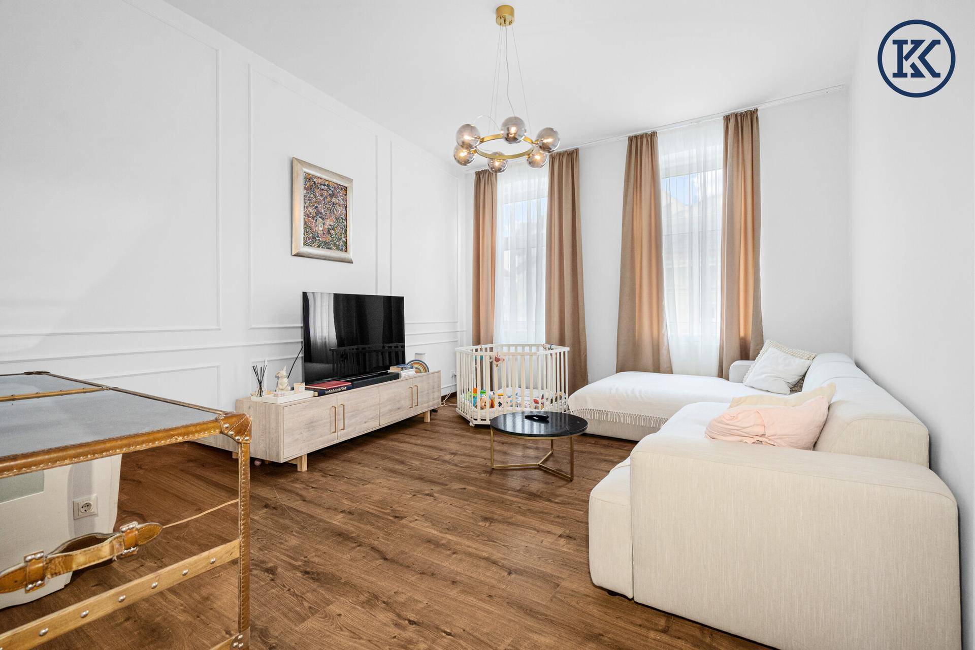 Gemütliches Wohnzimmer mit Holzboden, großem Sofa und einem Babybett in der Ecke.