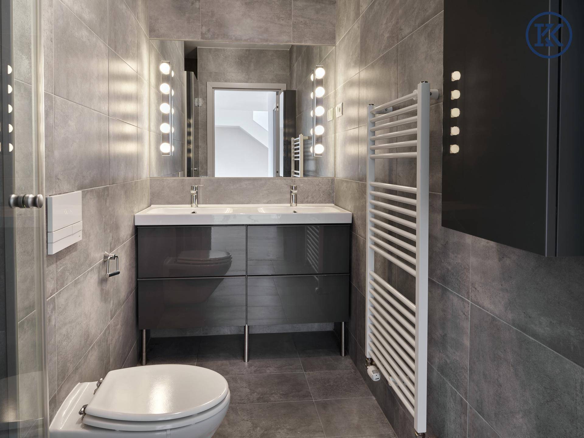Modernes Badezimmer mit Doppelwaschbecken, grauen Fliesen und beheiztem Handtuchhalter.