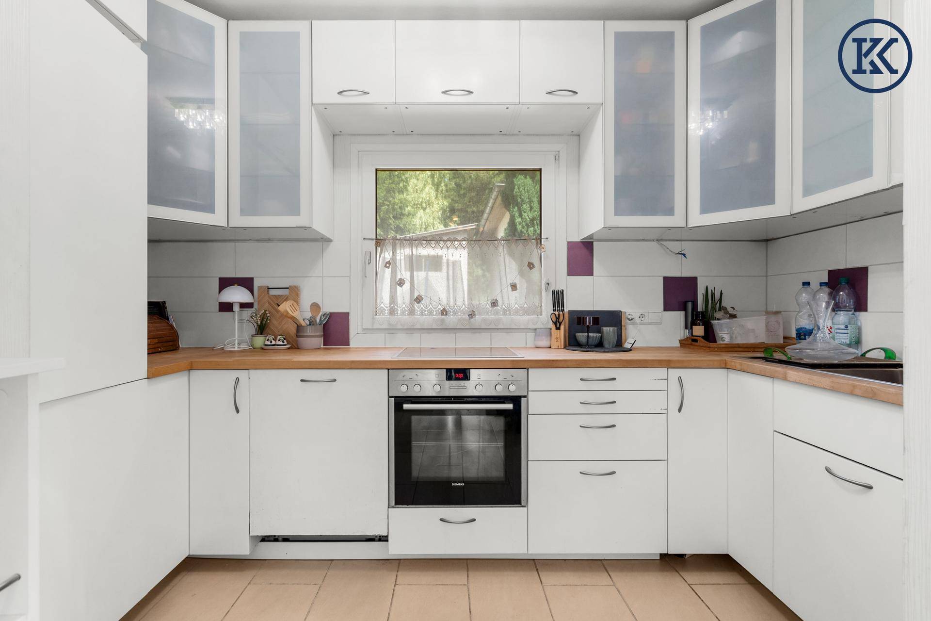 Funktionale Küche mit weißen Schränken, Holz-Arbeitsplatten und integriertem Backofen.