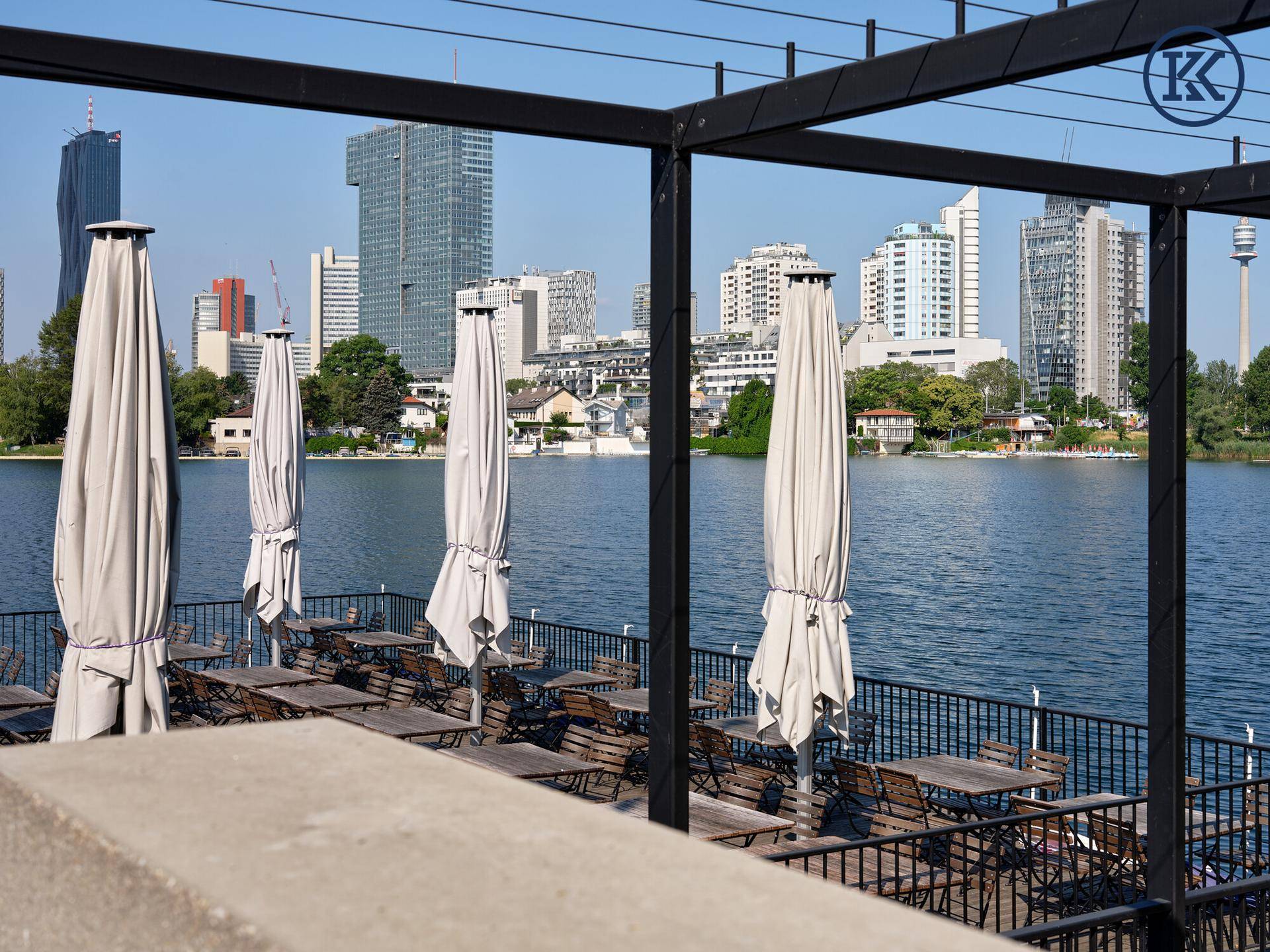 Gemütliche Seeterrasse mit Tischen, Stühlen und Sonnenschirmen, bietet einen direkten Blick auf die Stadtkulisse.