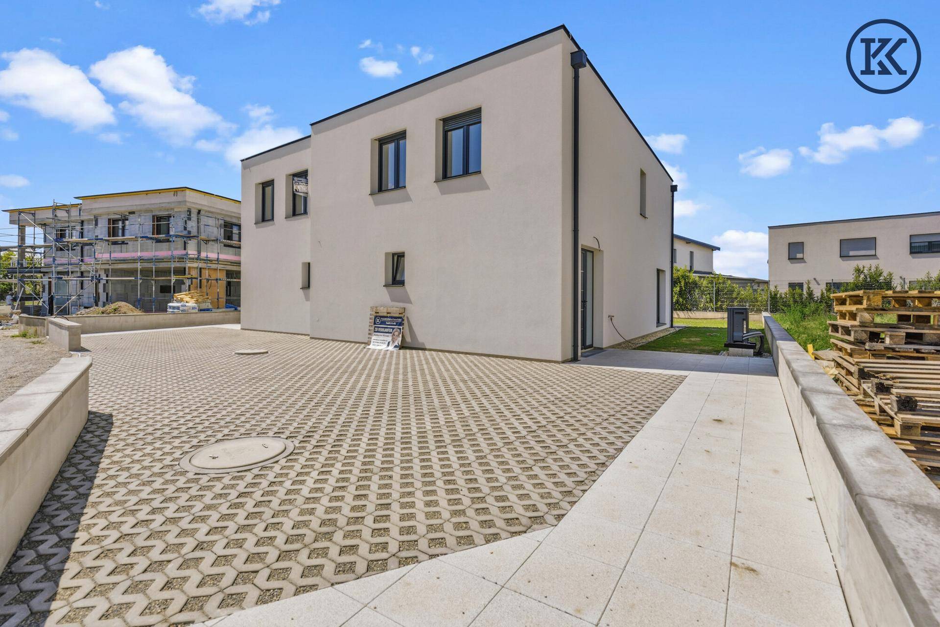 Außenansicht eines Neubaus mit gepflastertem Parkplatz und Baustellenumgebung.