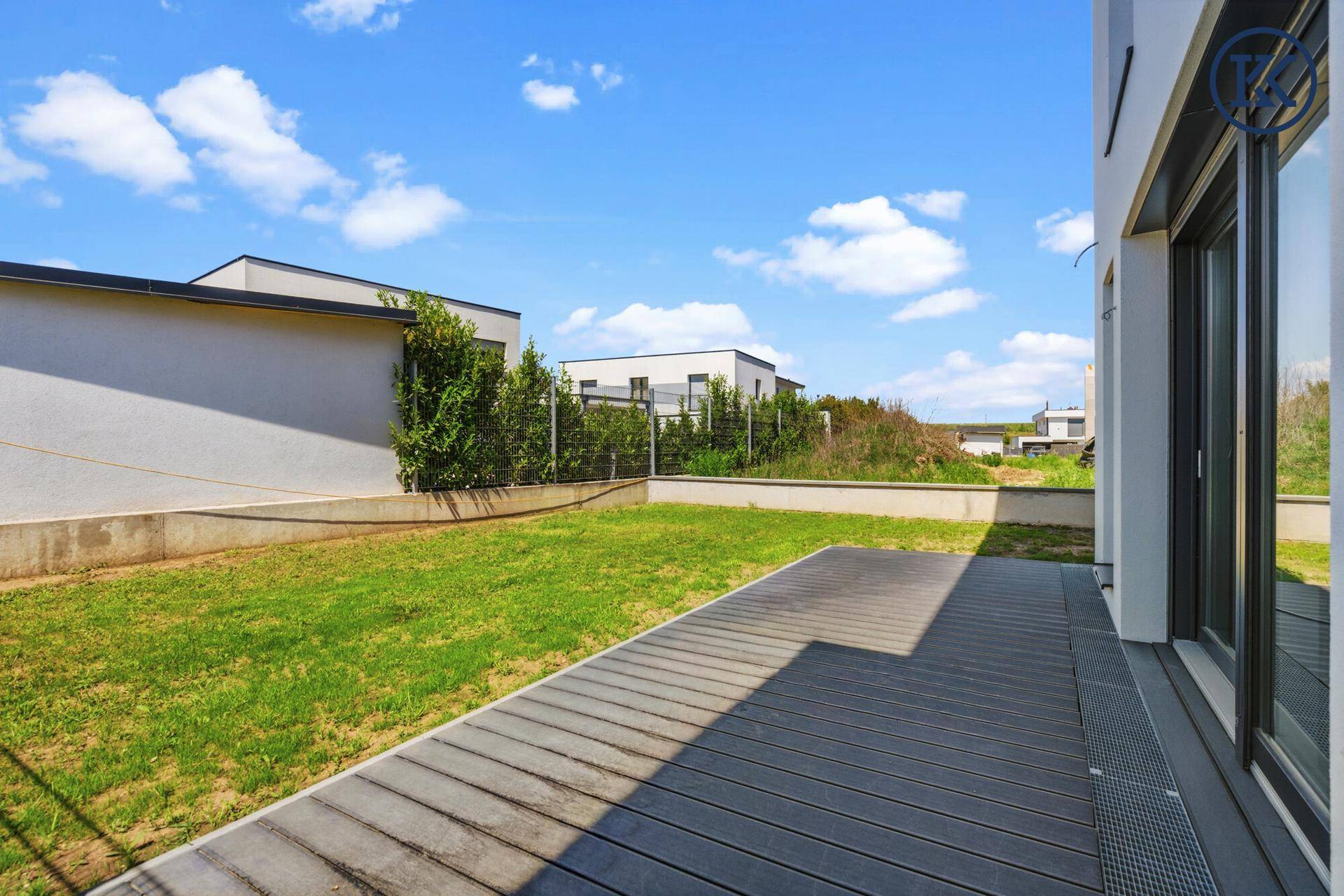 Gartenbereich mit Rasen und Holzterrasse, angrenzend an die moderne Hausfassade.