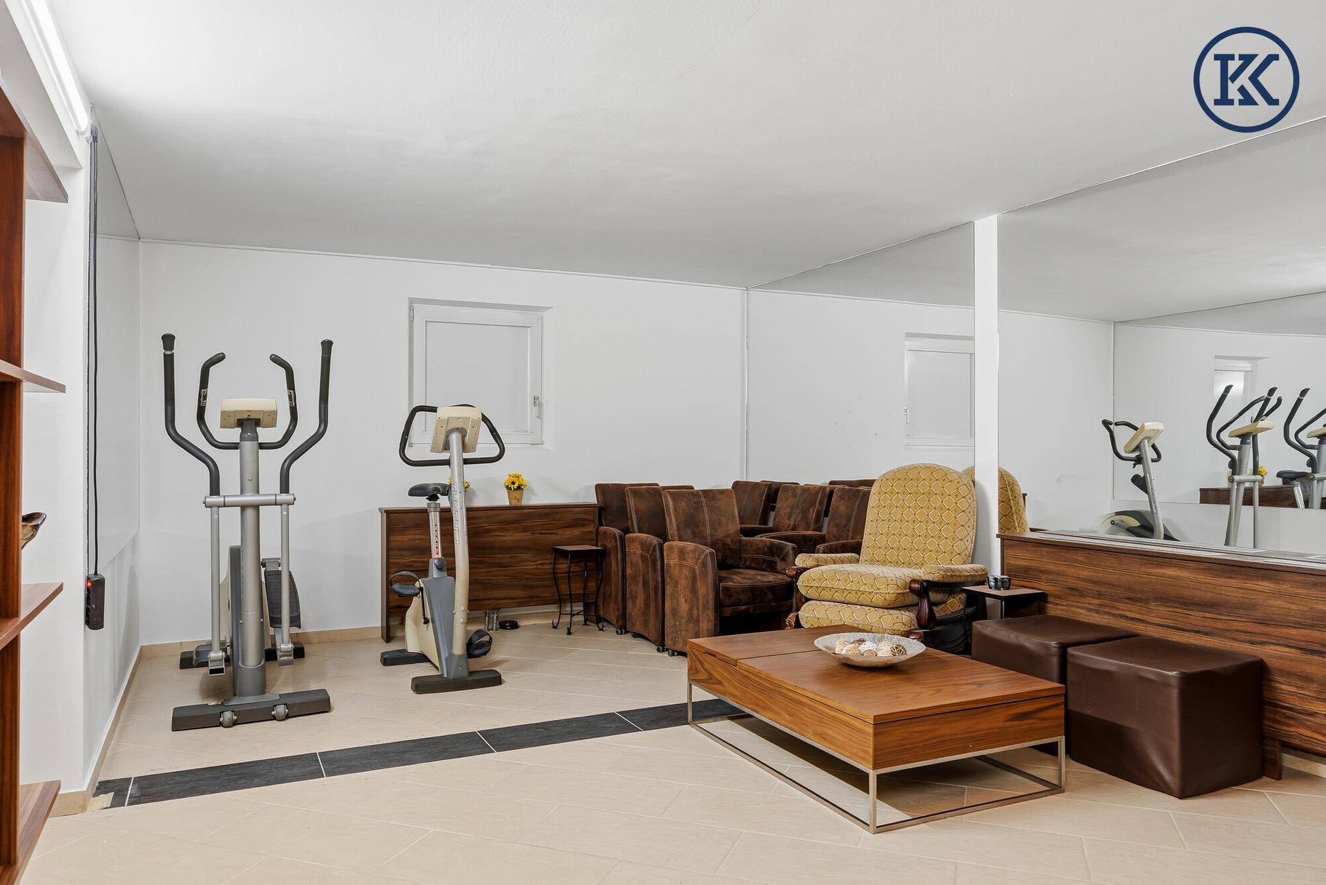 Fitnessraum im Untergeschoss mit Trainingsgeräten, Spiegeln und Sitzgelegenheiten.