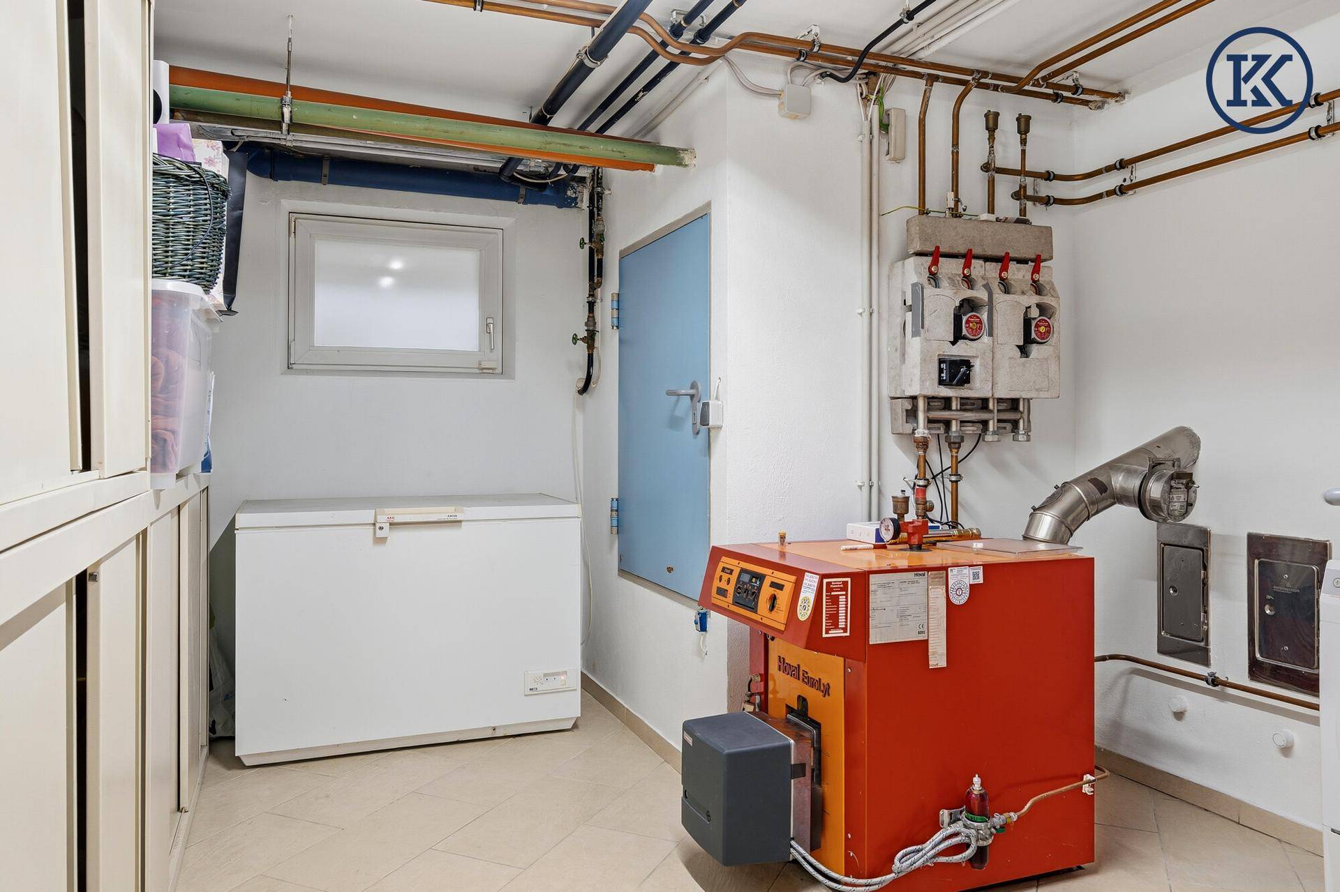 Heizungsraum mit Heizkessel, Rohren und einem Gefrierschrank im Keller.